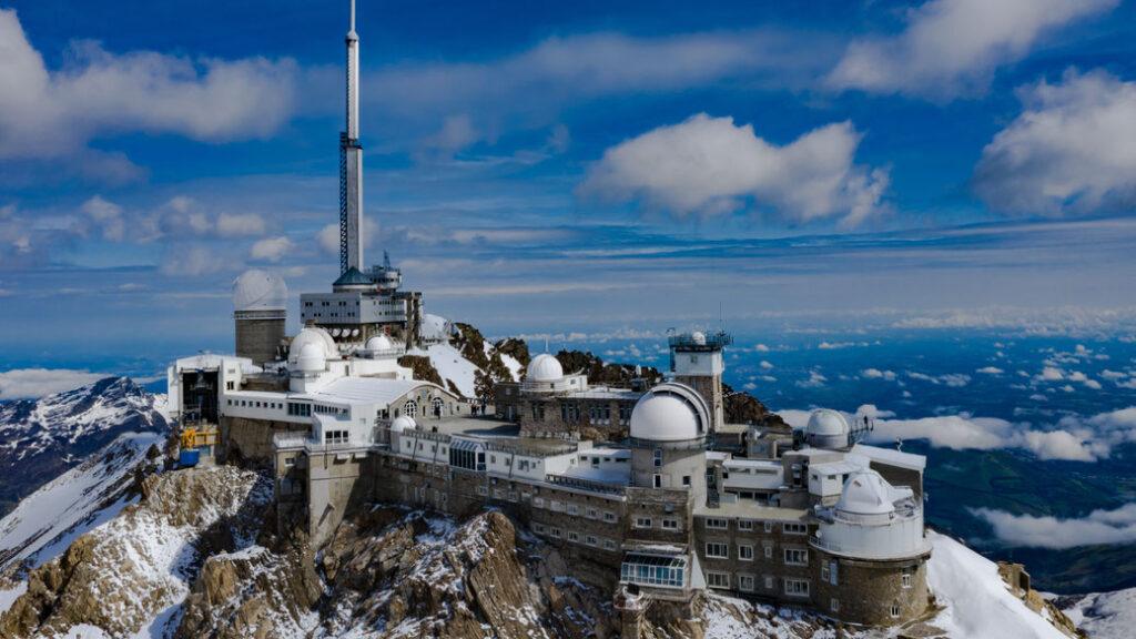 Observatorium auf schneebedecktem Berggipfel mit dramatischem Himmel im Hintergrund.