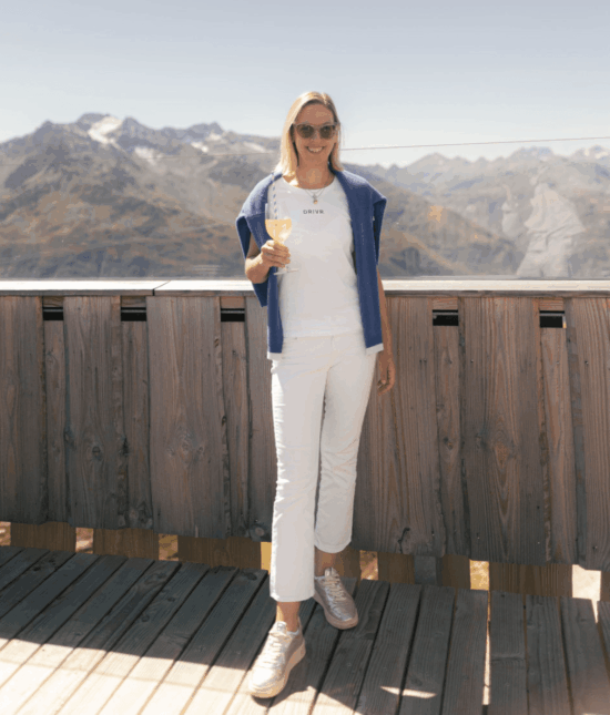 Frau genießt Weißwein vor Alpenpanorama auf einer Sportwagen Erlebnisreise.