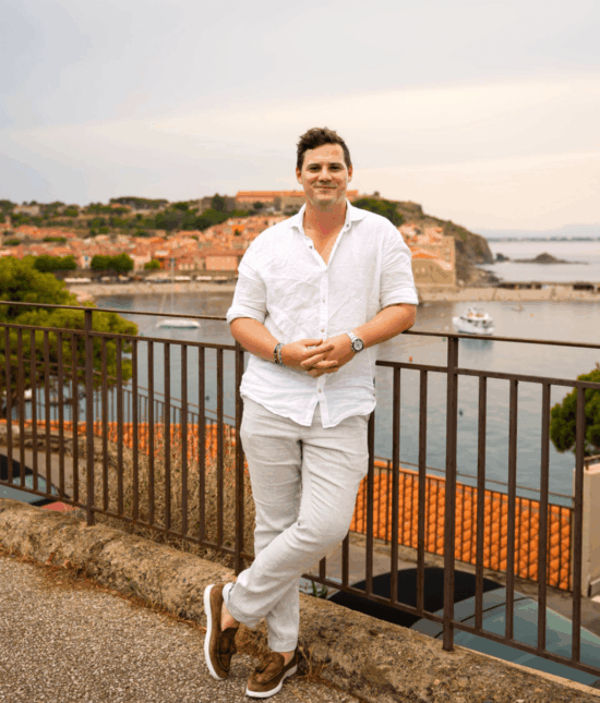 Mann in Leinenkleidung vor mediterraner Küstenstadt während einer Sportwagen Erlebnisreise.