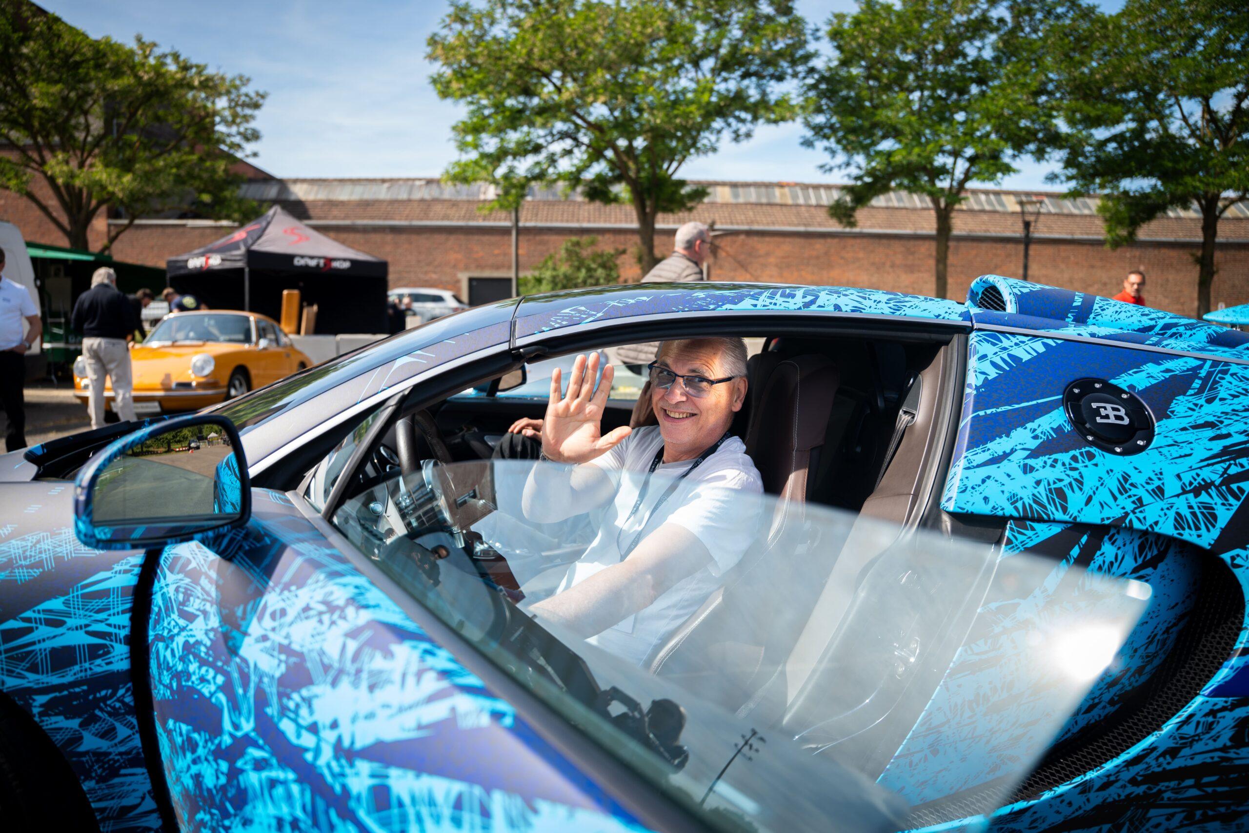 Sportwagen Erlebnisreisen: Glücklicher Teilnehmer winkt aus einem blauen Bugatti Cabrio während der Tour.