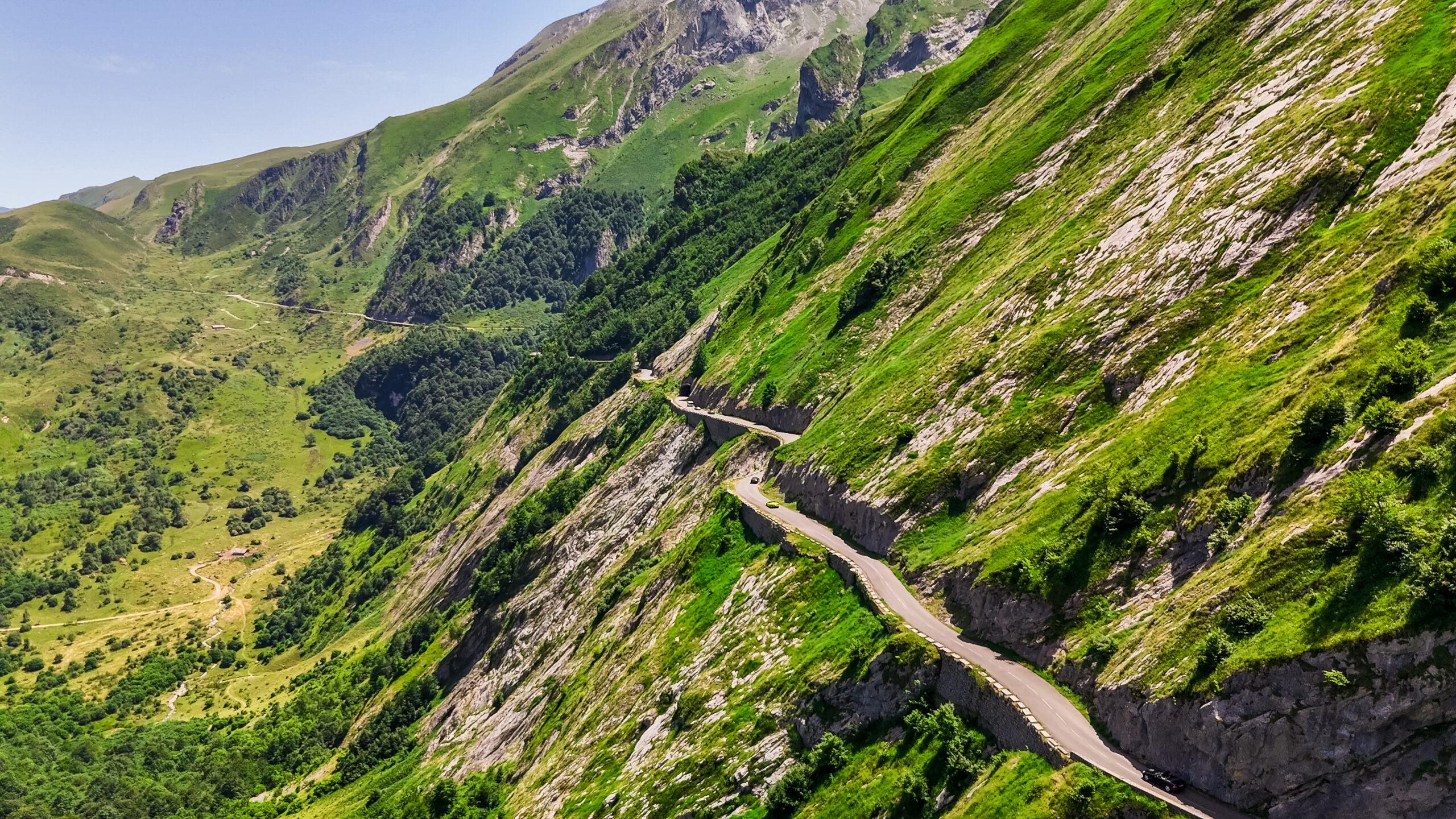 Bergstraße windet sich durch grüne Hänge in den Alpen. Abenteuerlicher Fahrspaß.