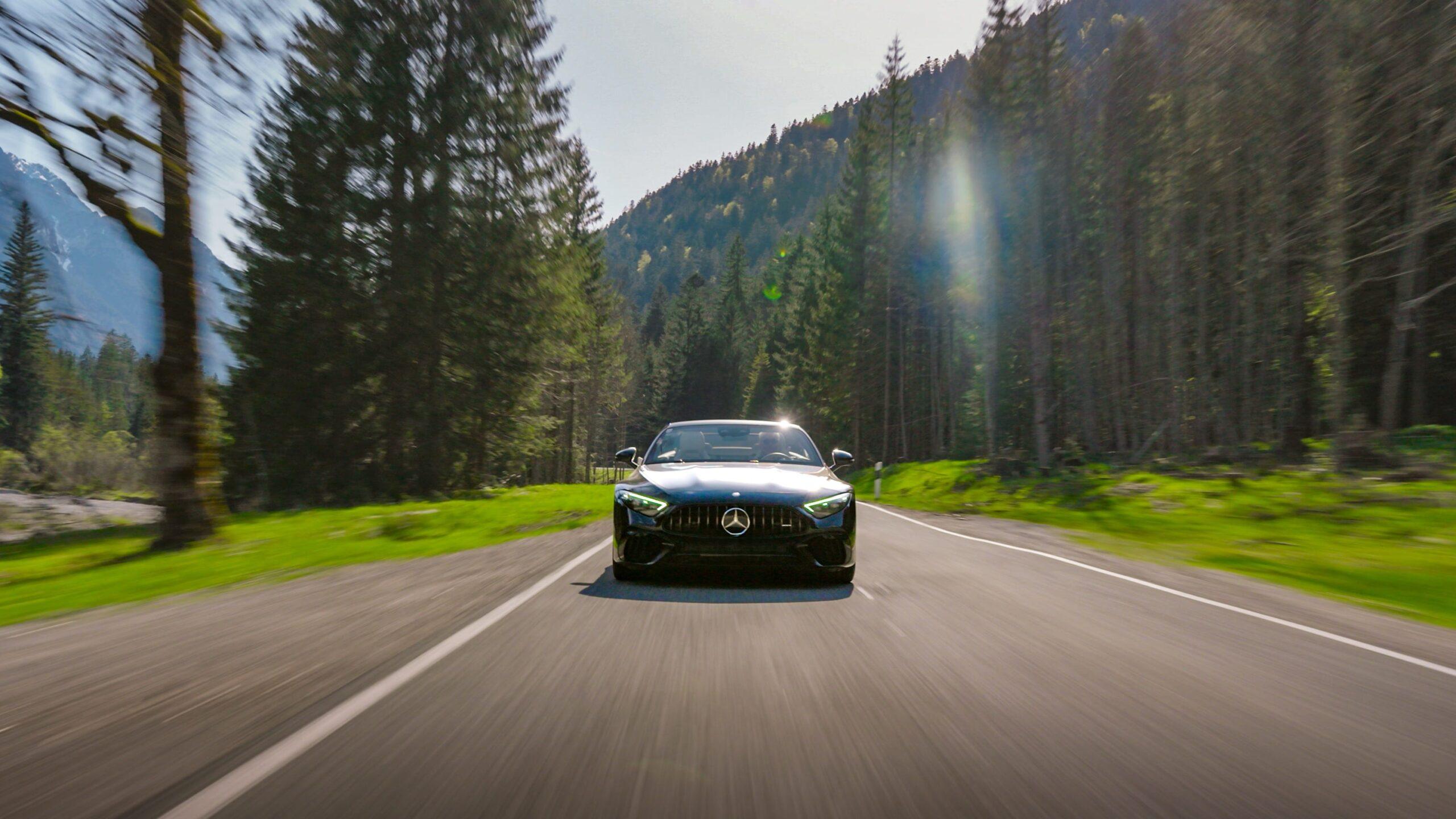 Sportwagen fährt auf einer malerischen Straße durch den dichten Wald der Alpen.