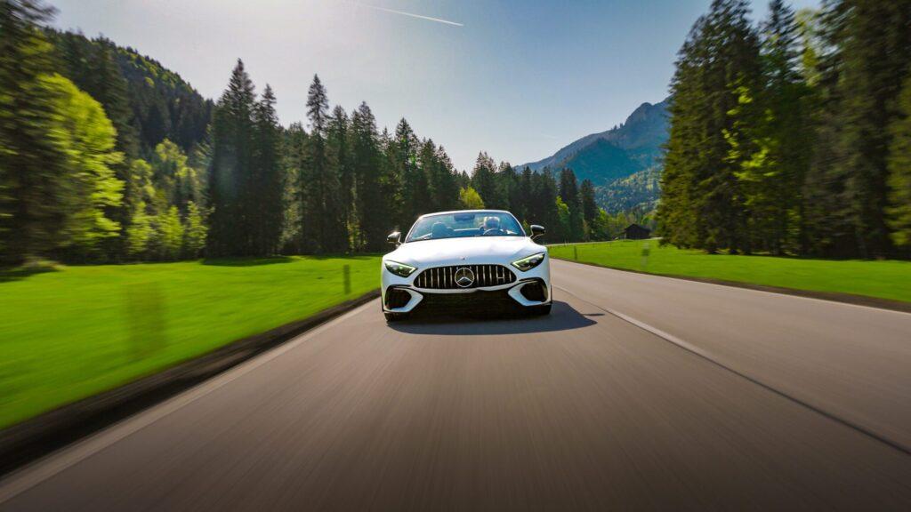 Ein eleganter Sportwagen fährt durch grüne Wiesen, umgeben von majestätischen Bergen und Nadelbäumen.