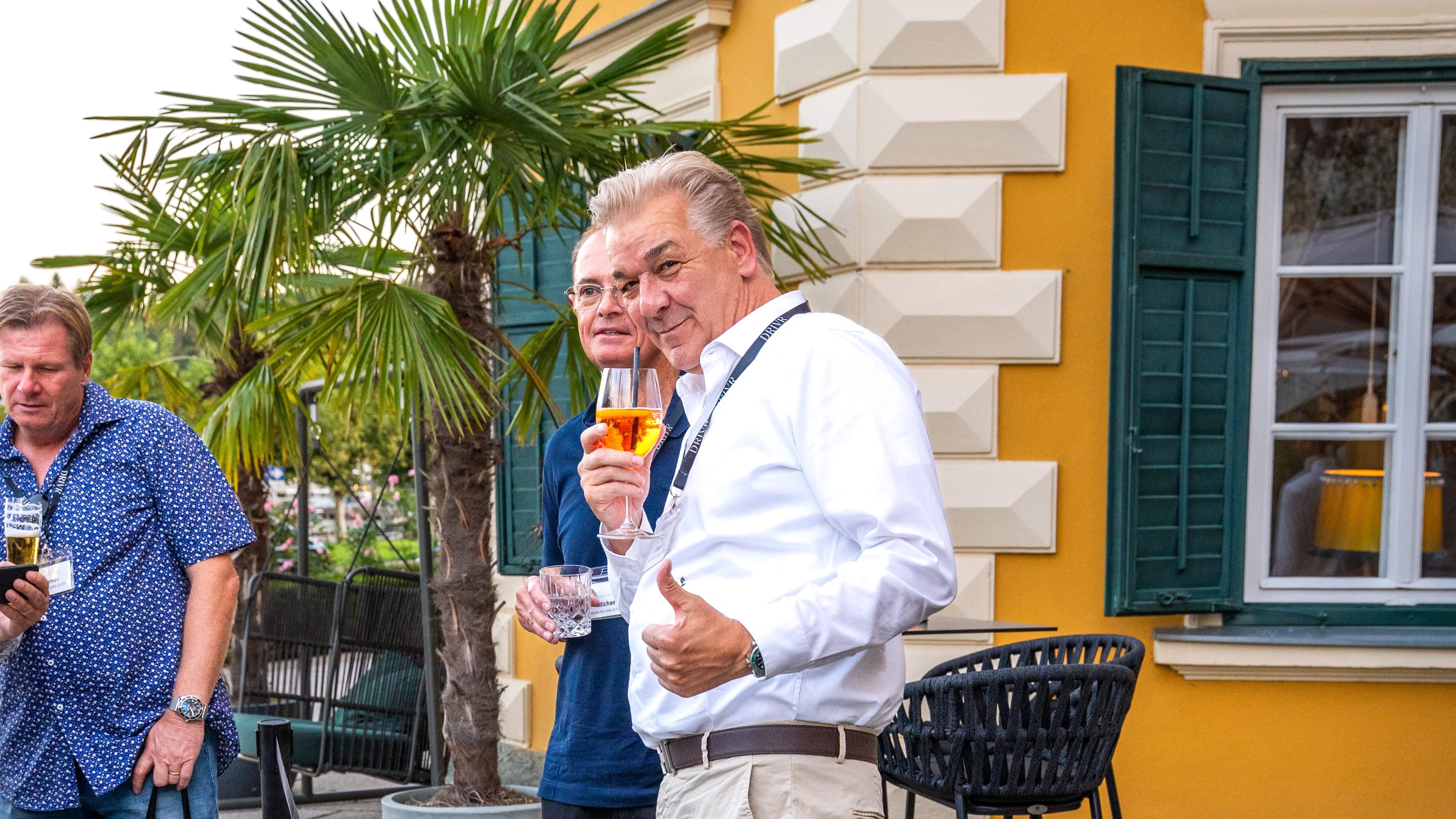 Männer genießen Getränke in einem Hotelgarten während einer Luxusautotour in Europa.