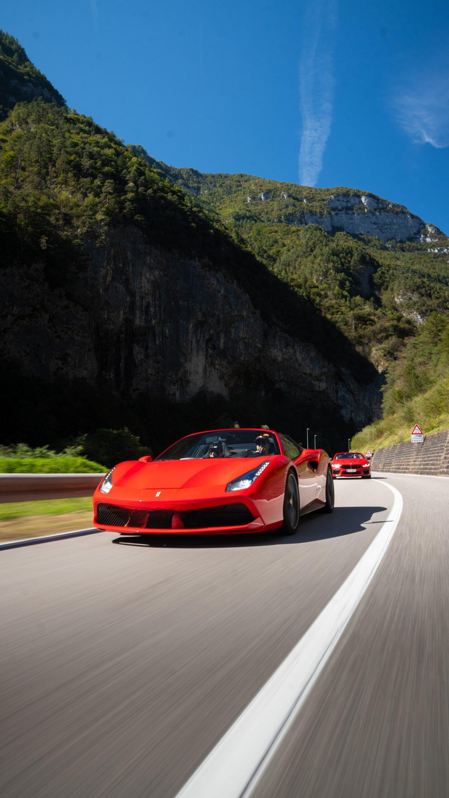 Sportwagen Erlebnisreisen: Roter Ferrari in dynamischer Fahrt auf einer Bergstraße vor Felskulisse.