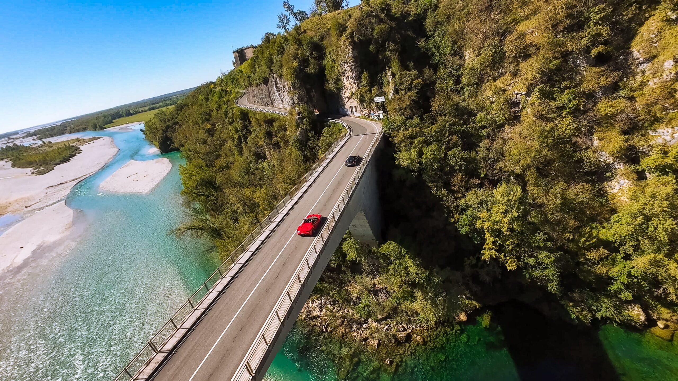 Sportwagen fahren über malerische Brücke mit türkisfarbenem Fluss darunter.
