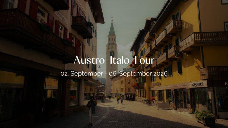 Header Bild der Austro-Italo Tour: Dorfzentrum mit hohem Kirchturm und Gasse in den Alpen.