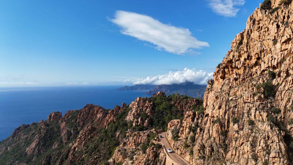 Zwei Sportwagen fahren entlang einer spektakulären Küstenstraße im Gebirge.