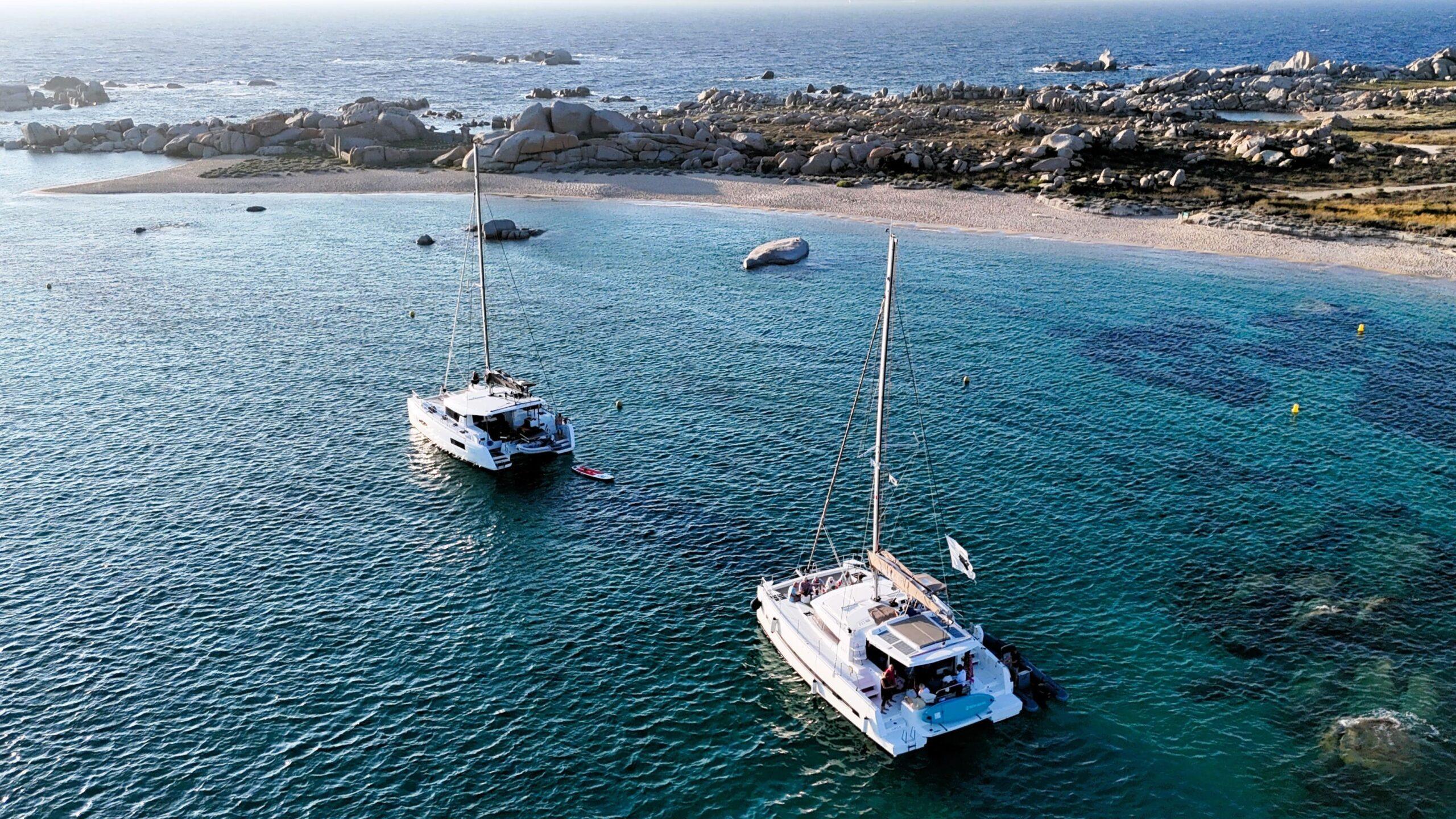 Zwei Yachten vor einer malerischen Küste in kristallklarem Wasser.