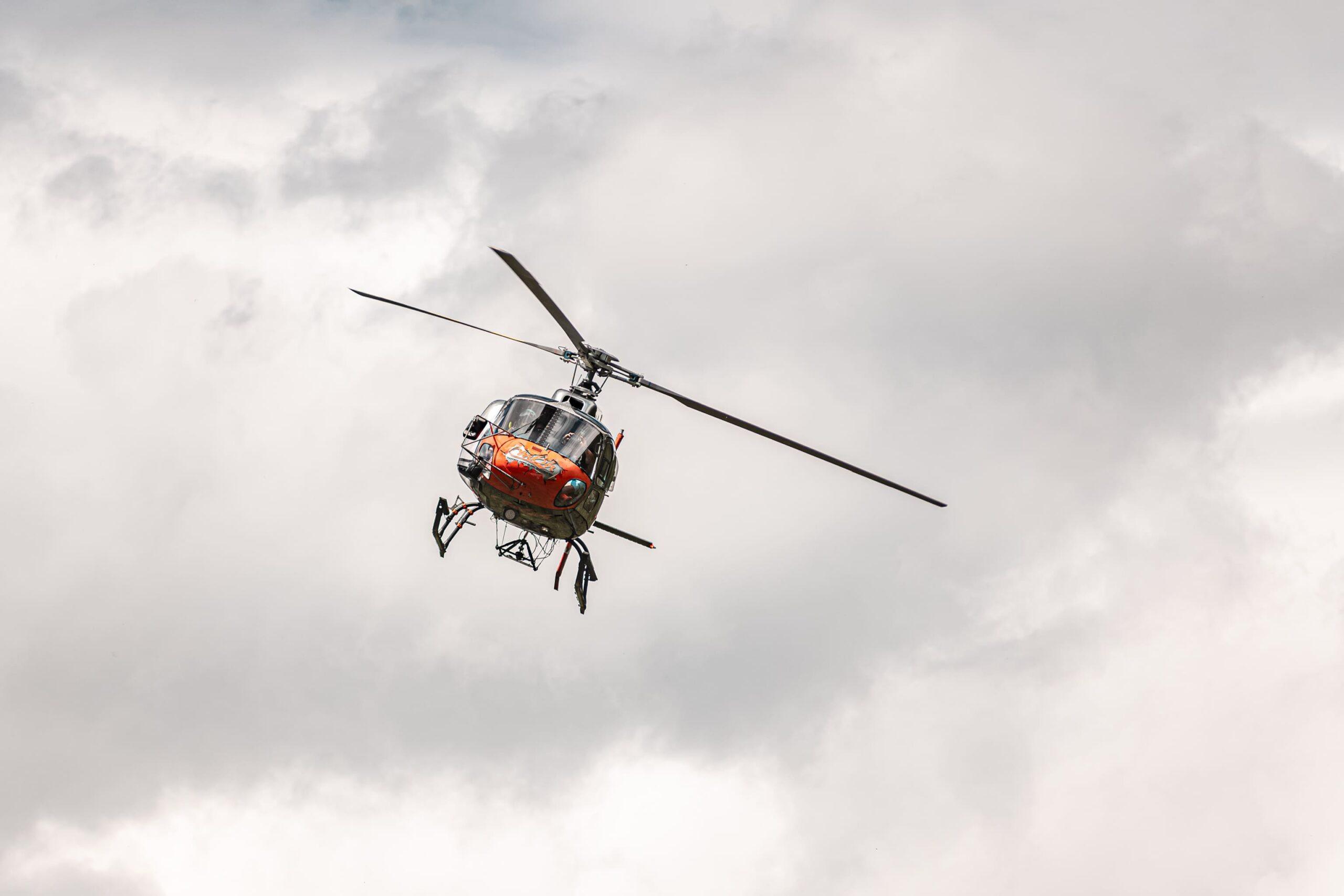 Ein roter Hubschrauber fliegt durch bewölkten Himmel in den Alpen.