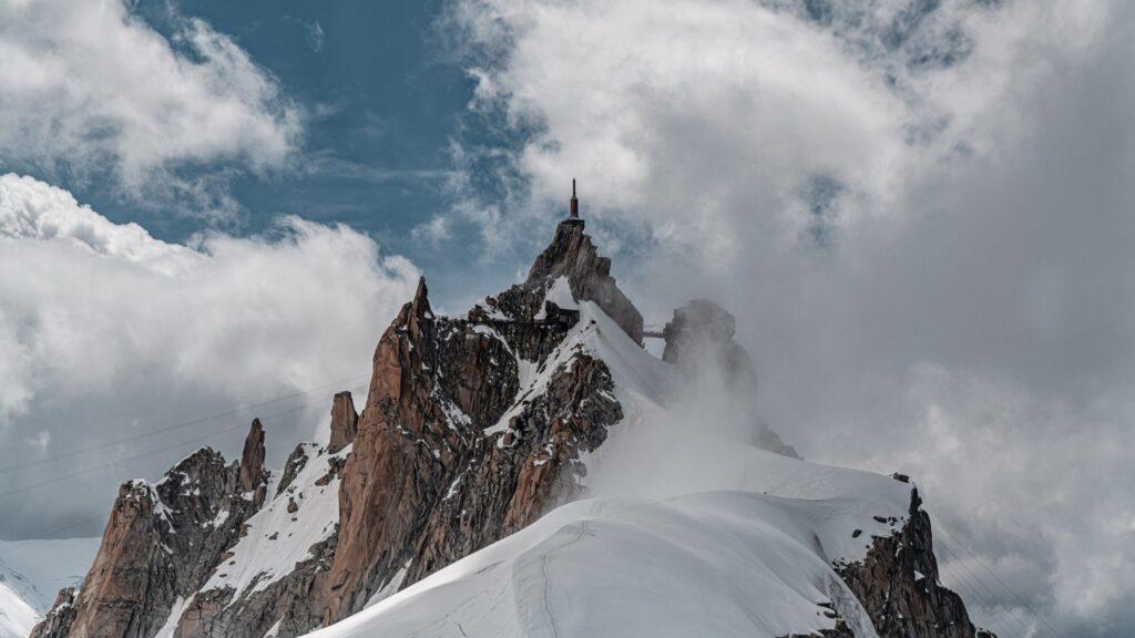 Beeindruckender Berggipfel mit schneebedeckten Hängen und dramatischer Wolkenkulisse in den Alpen.