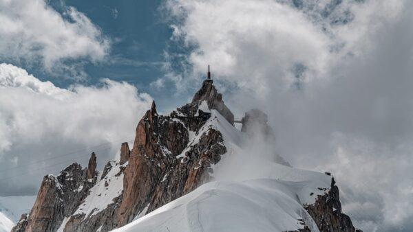 Beeindruckender Berggipfel mit schneebedeckten Hängen und dramatischer Wolkenkulisse in den Alpen.