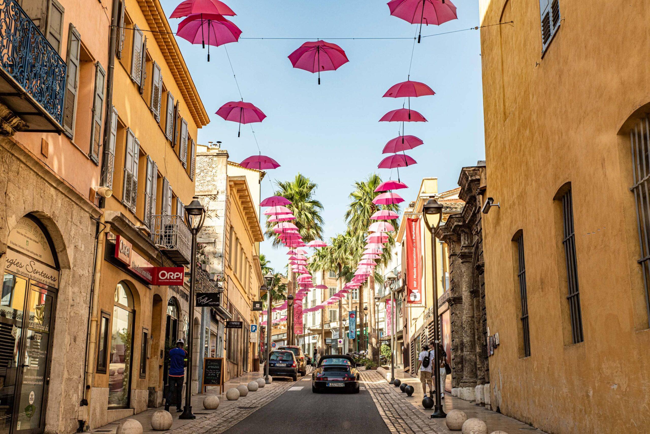 Sportwagen fährt durch malerische Straßen mit hängenden rosa Regenschirmen in Südfrankreich.