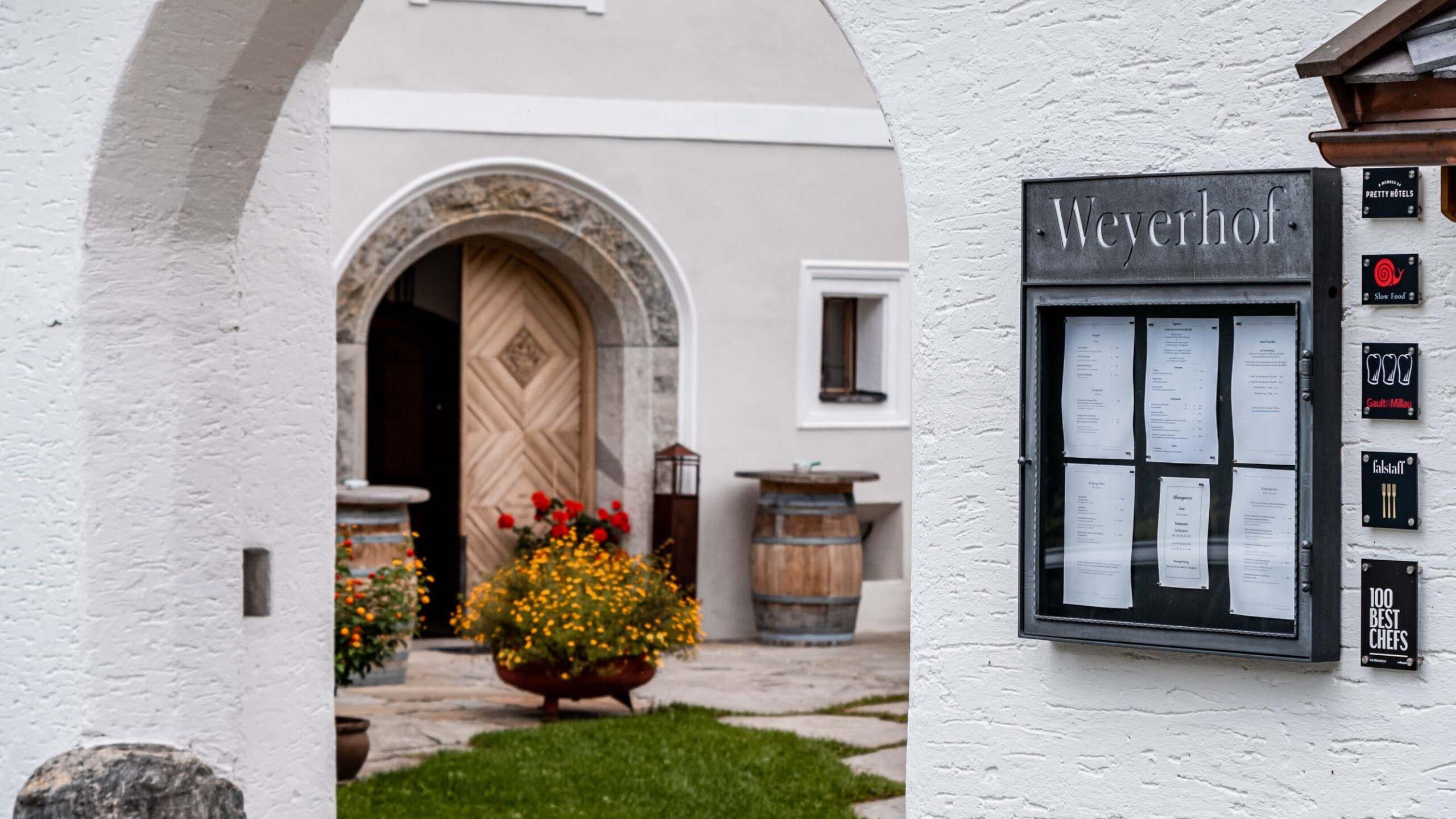 Eingang zu einem eleganten Hotel mit Blumendekoration und Holzfass in den Alpen.