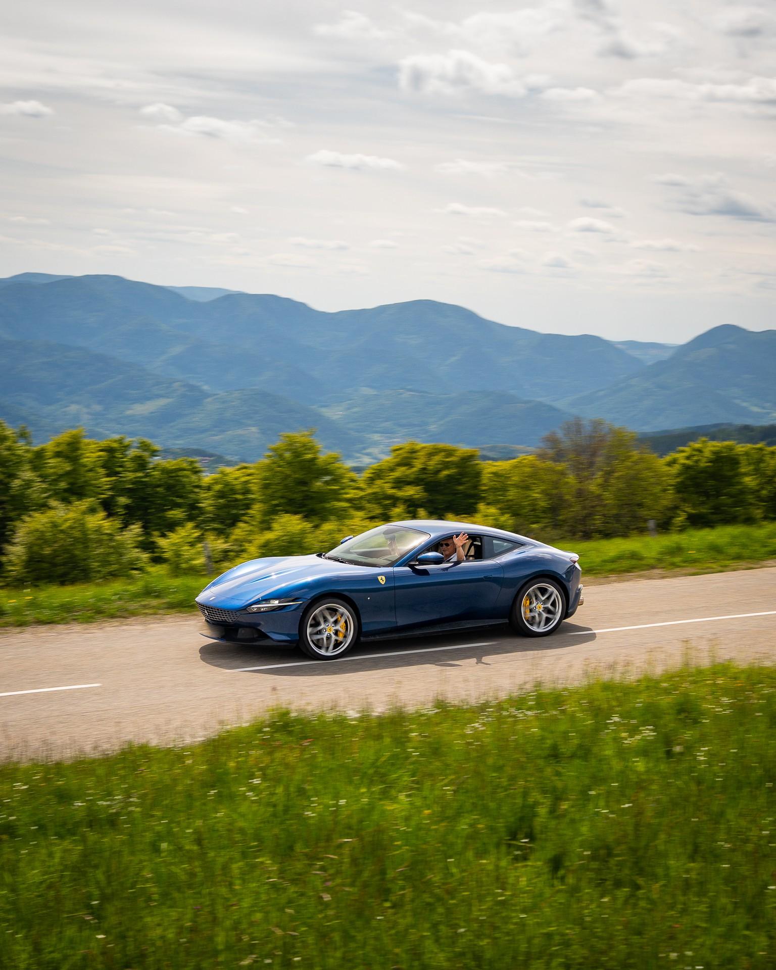 Sportwagen Erlebnisreisen: Blauer Ferrari Roma fährt auf einer Panoramastraße durch die grüne Landschaft des Elsass.