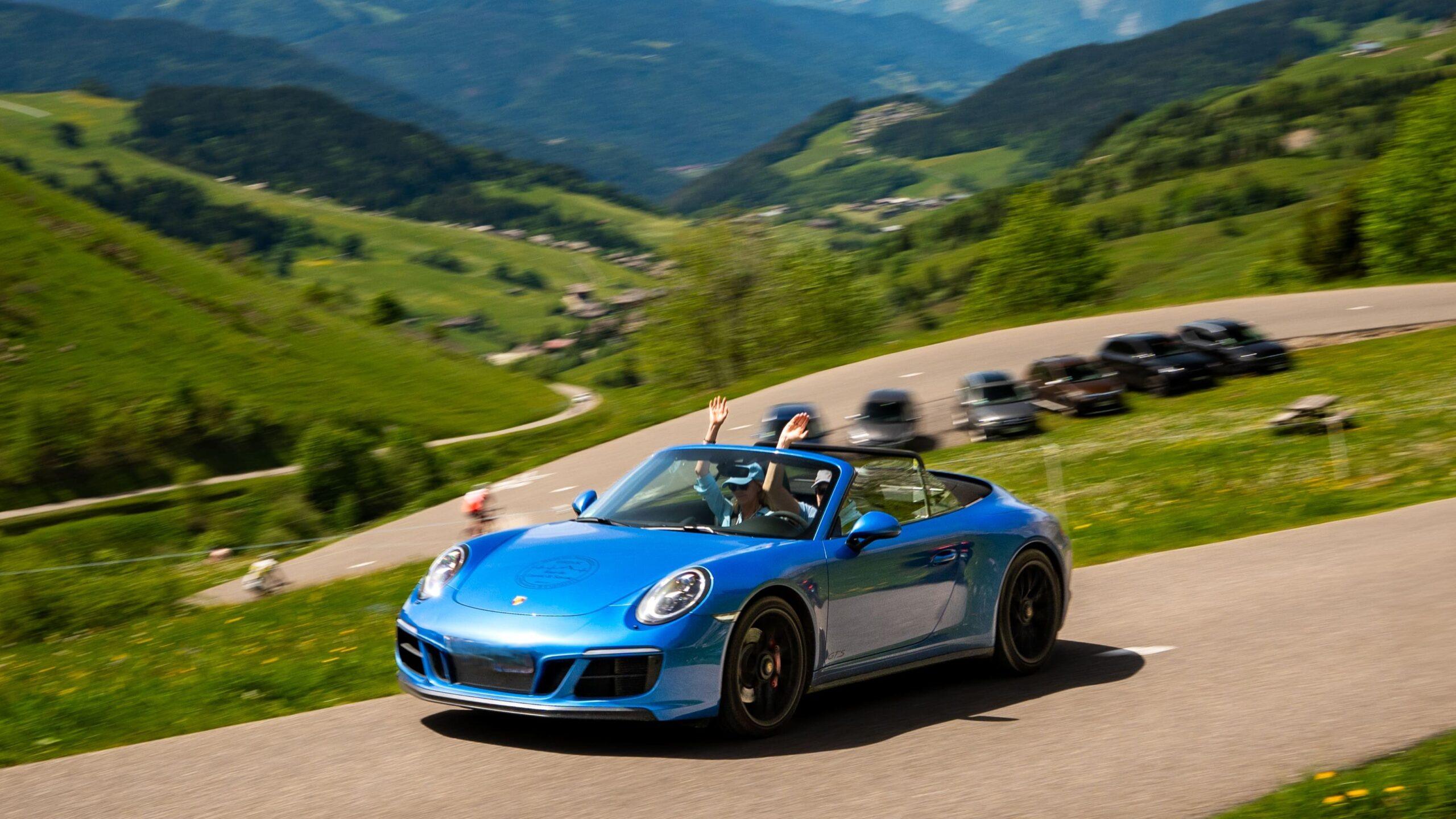 Blauer Sportwagen fährt durch malerische Bergstraßen im Sommer.