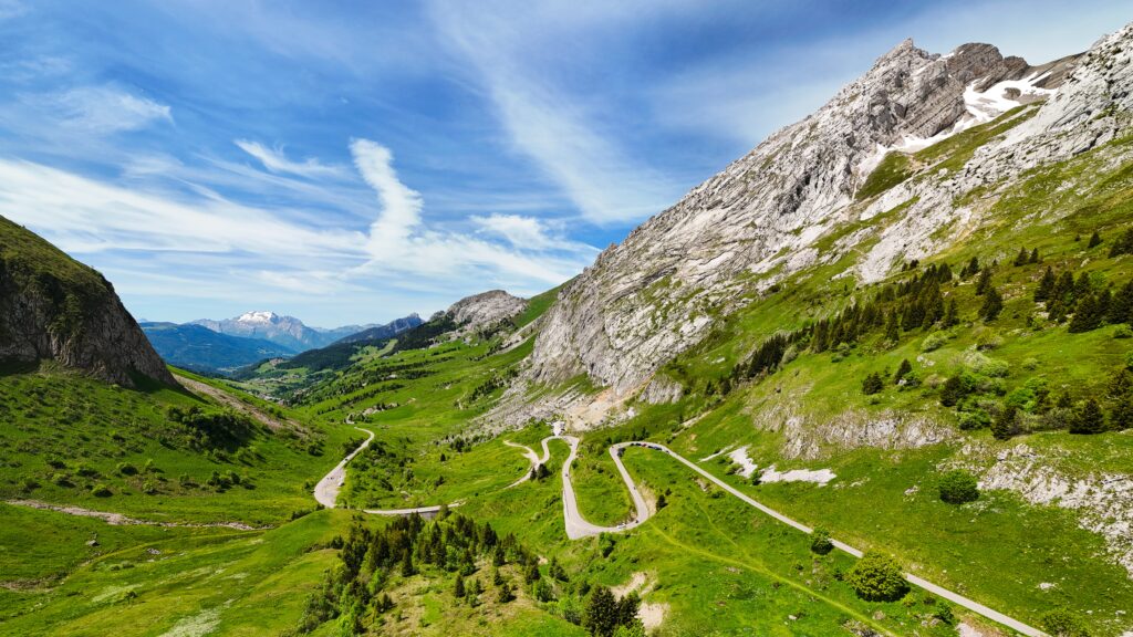 Kurvige Bergstraße in den Alpen, umgeben von grünen Wiesen und majestätischen Gipfeln.