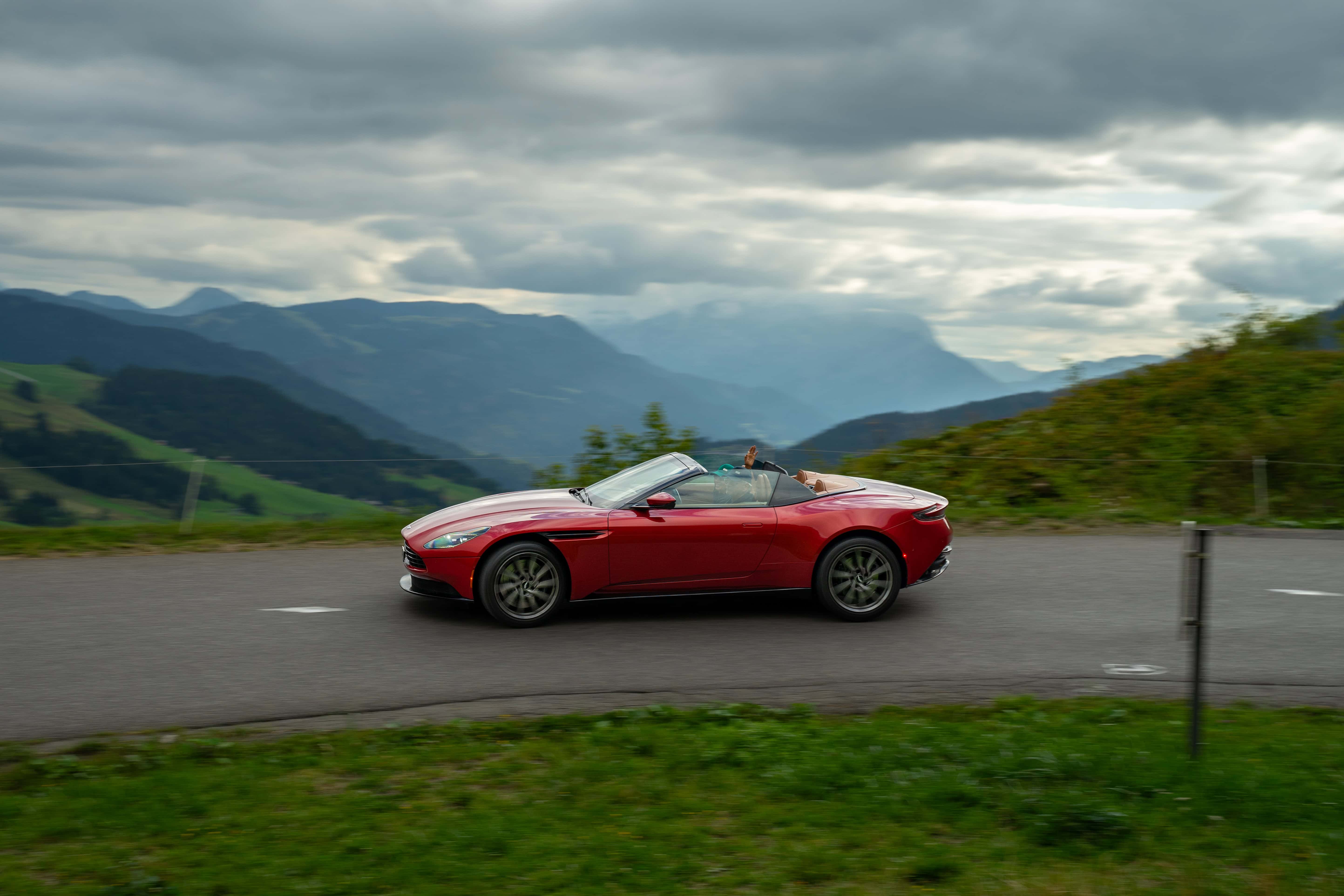 Roter Sportwagen fährt durch malerische Alpenlandschaft bei bedecktem Himmel.