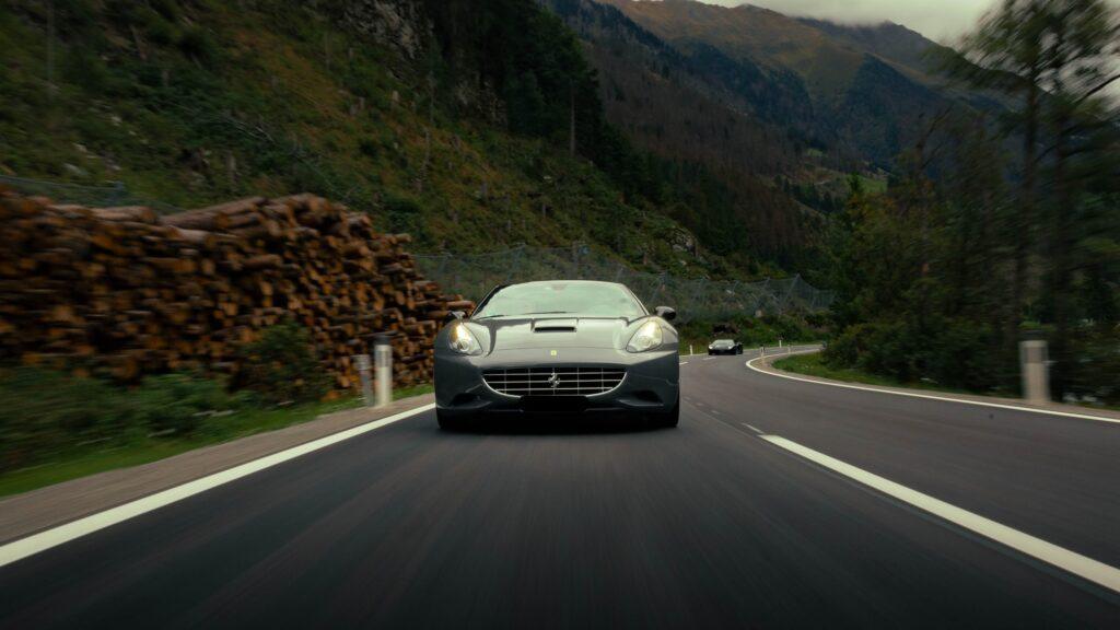 Silbergrauer Sportwagen fährt auf kurvenreicher Bergstraße in den Alpen.