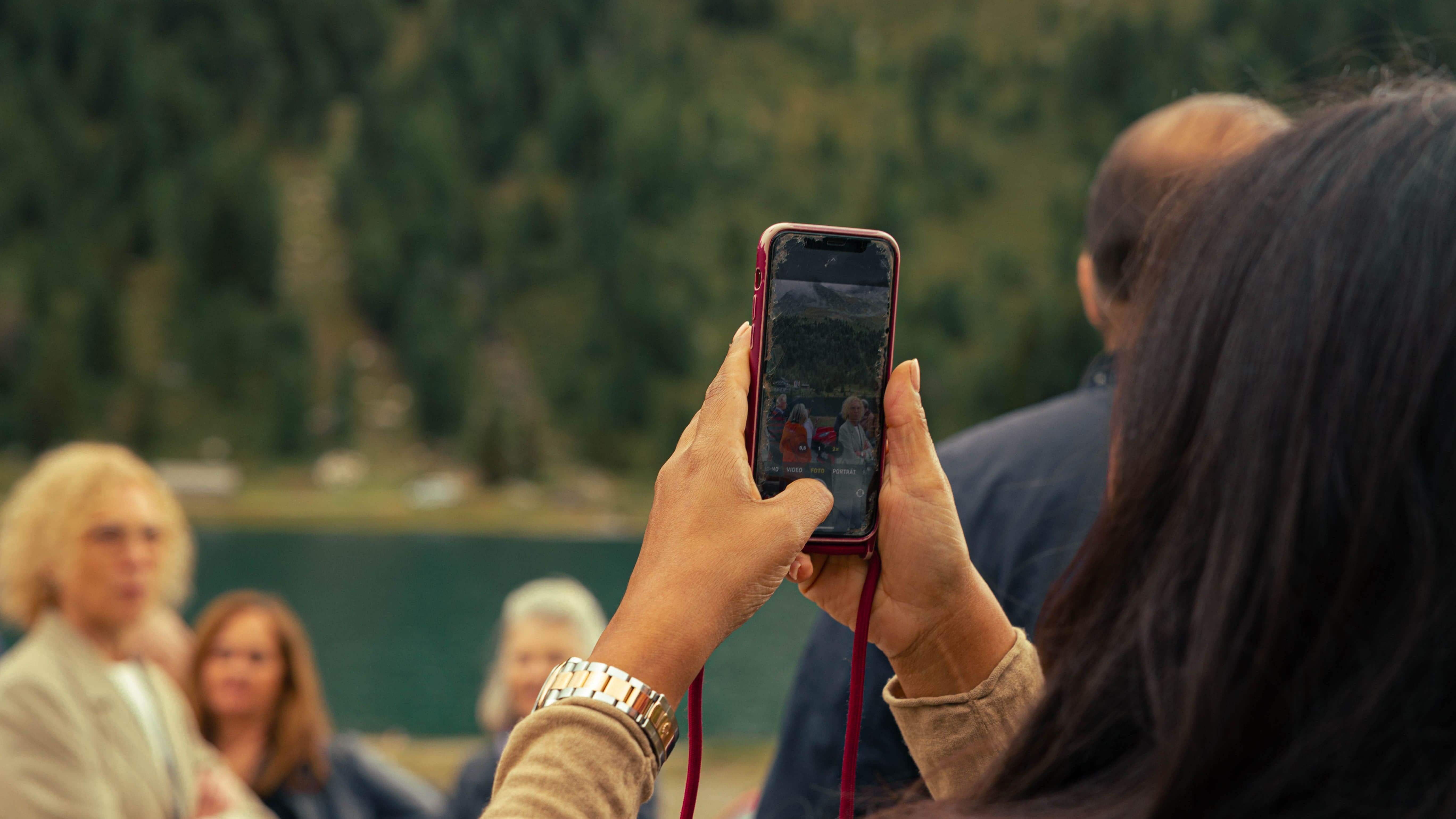 Frau fotografiert malerische Alpenlandschaft mit dem Smartphone im Hintergrund.