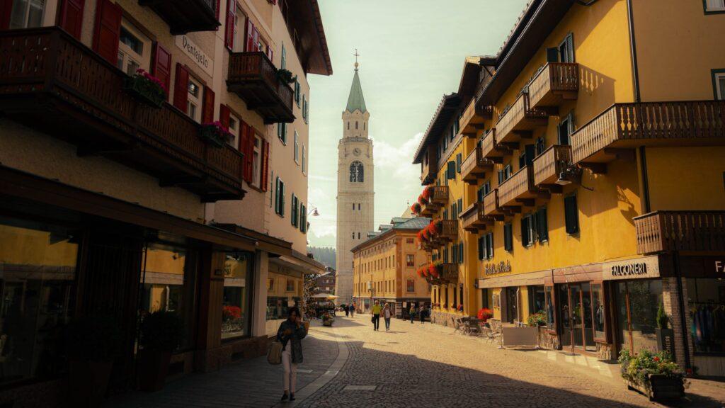 Straße in den Dolomiten mit historischen Gebäuden und charmantem Turm im Hintergrund.