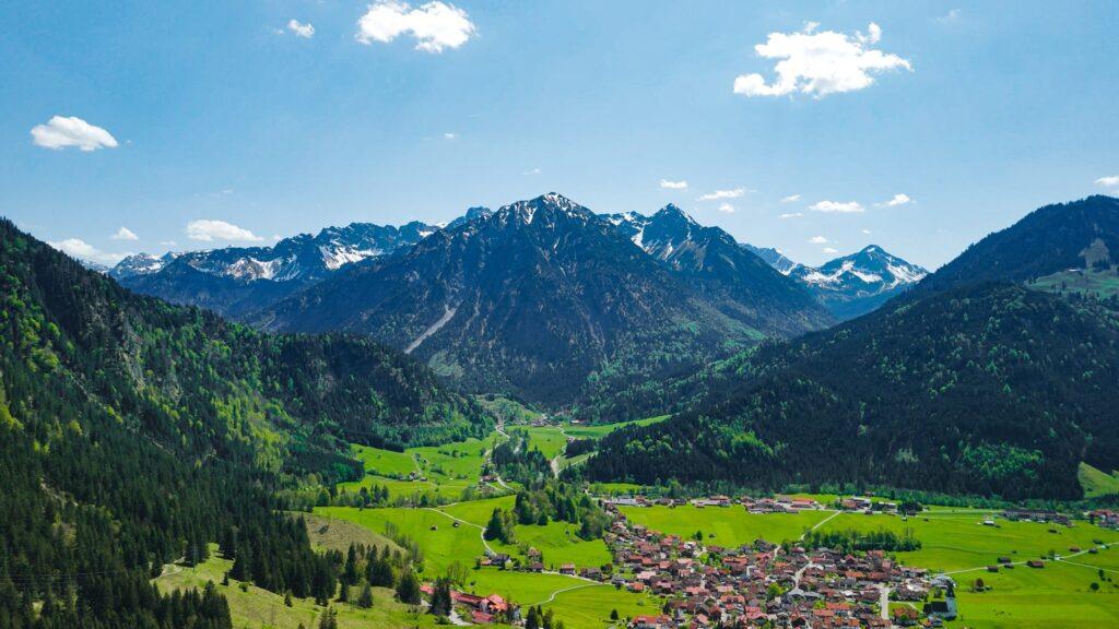 Alpenpanorama mit grünen Tälern und schneebedeckten Gipfeln bei klarem Himmel.