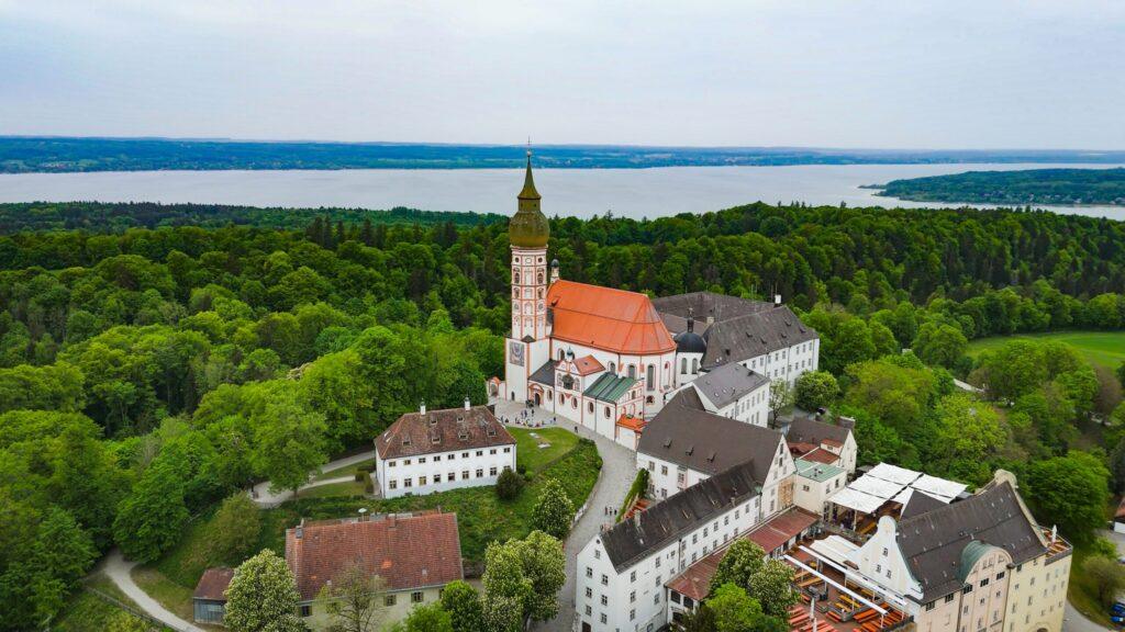 Luftbild einer malerischen Klosterkirche in üppiger grüner Landschaft am See.