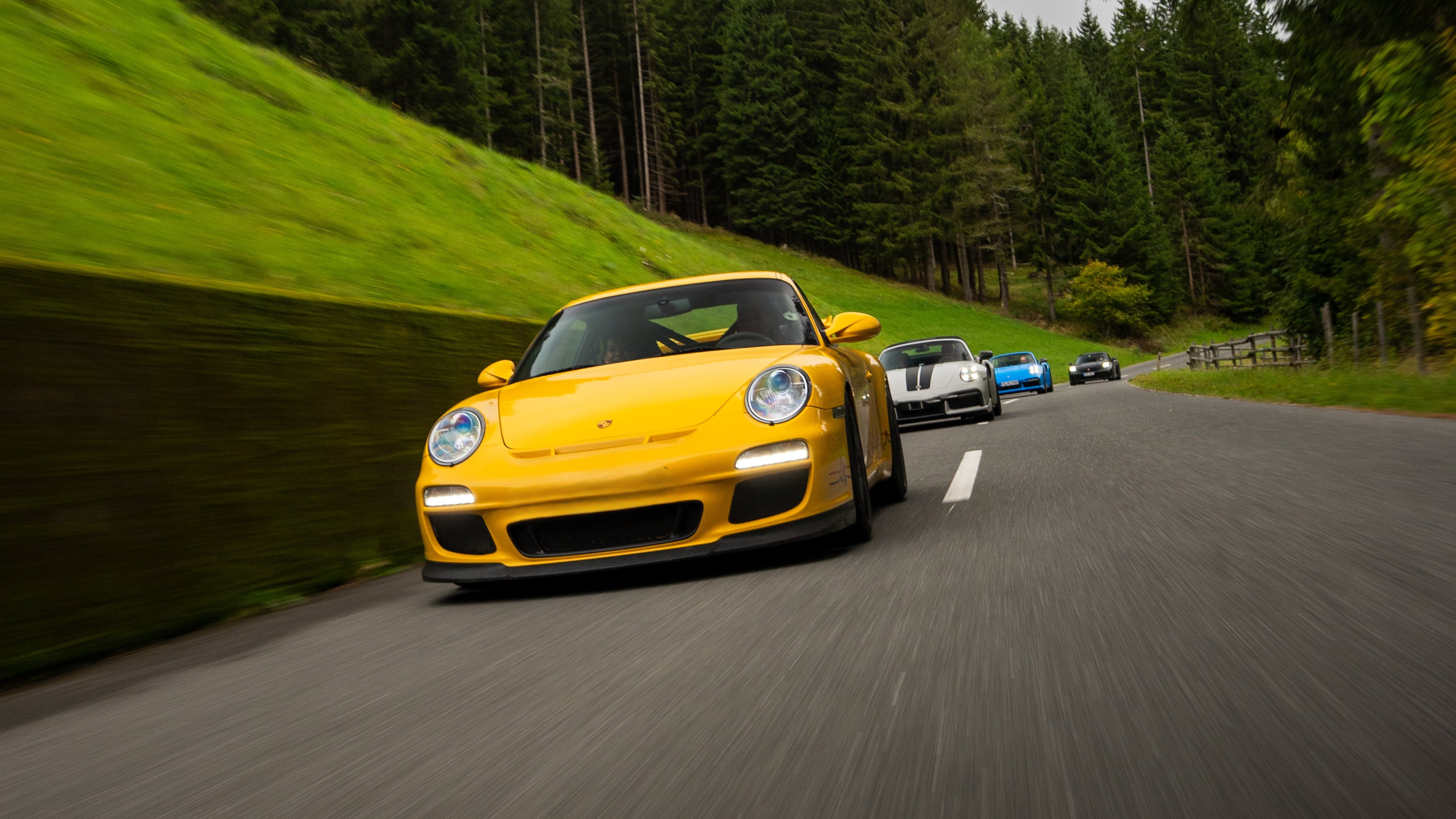 Gelber Sportwagen führt Autokolonne auf malerischer Straße im Schwarzwald an.