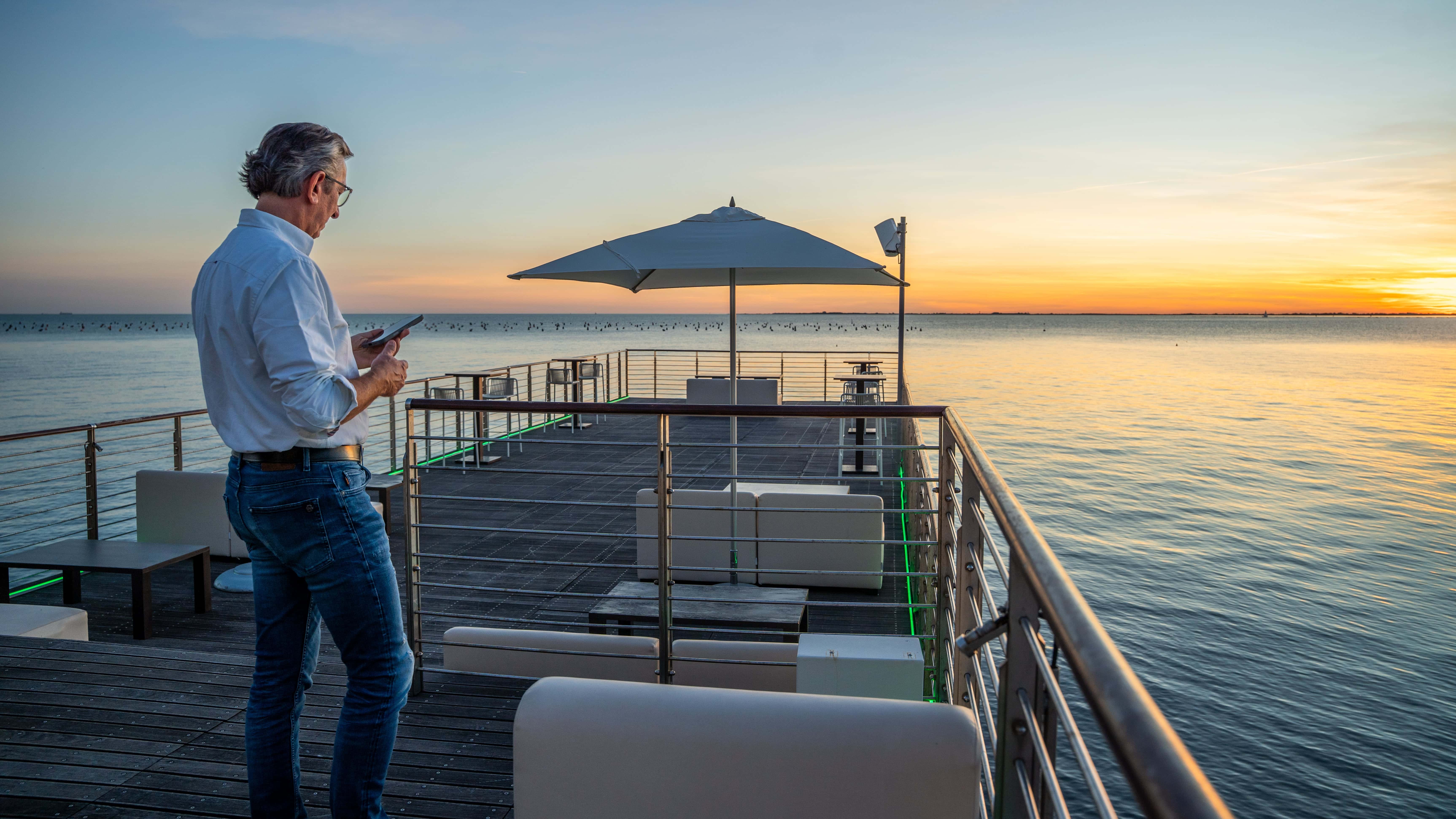 Mann genießt Sonnenuntergang auf Terrasse am Meer während einer Luxusreise.