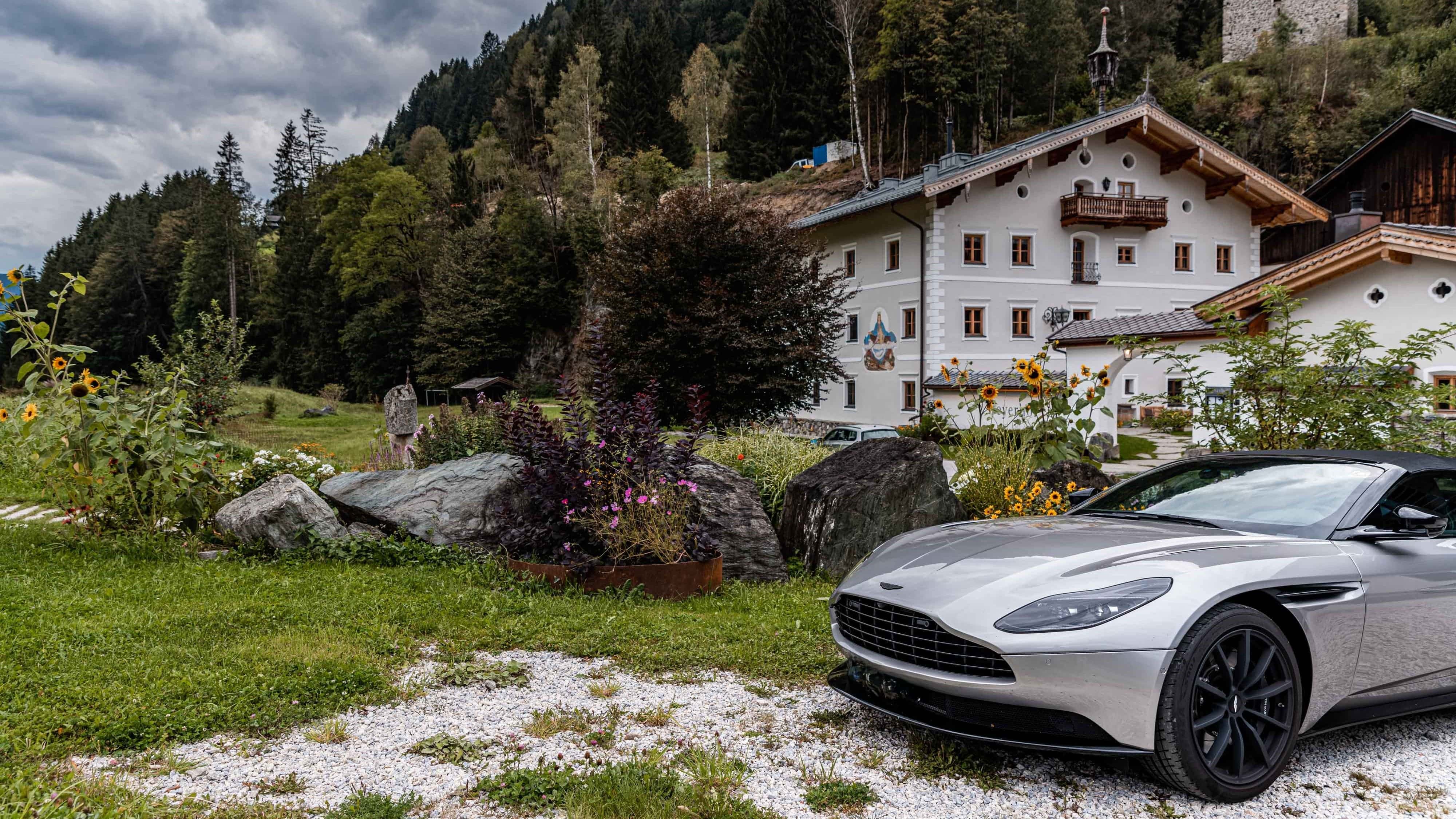 Silberner Sportwagen vor alpinem Gasthaus in idyllischer Berglandschaft.