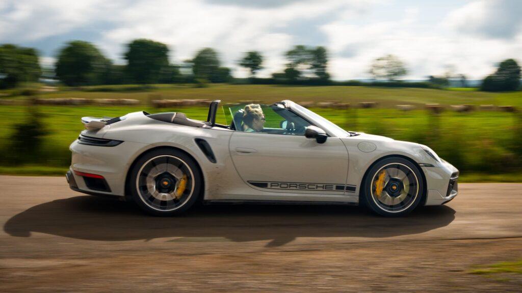 Weißer Sportwagen fährt zügig durch malerische Landschaft, Fahrer genießt die Fahrt.