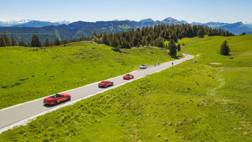 Eine Karawane von Sportwagen fährt auf einer malerischen Alpenstraße.