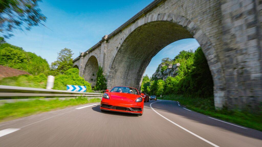 Rotes Cabrio fährt dynamisch auf einer kurvigen Straße unter einer Steinbrücke.