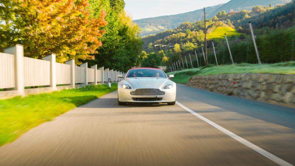 Weißer Sportwagen fährt durch malerische Landschaft der Dolomiten im Herbst.