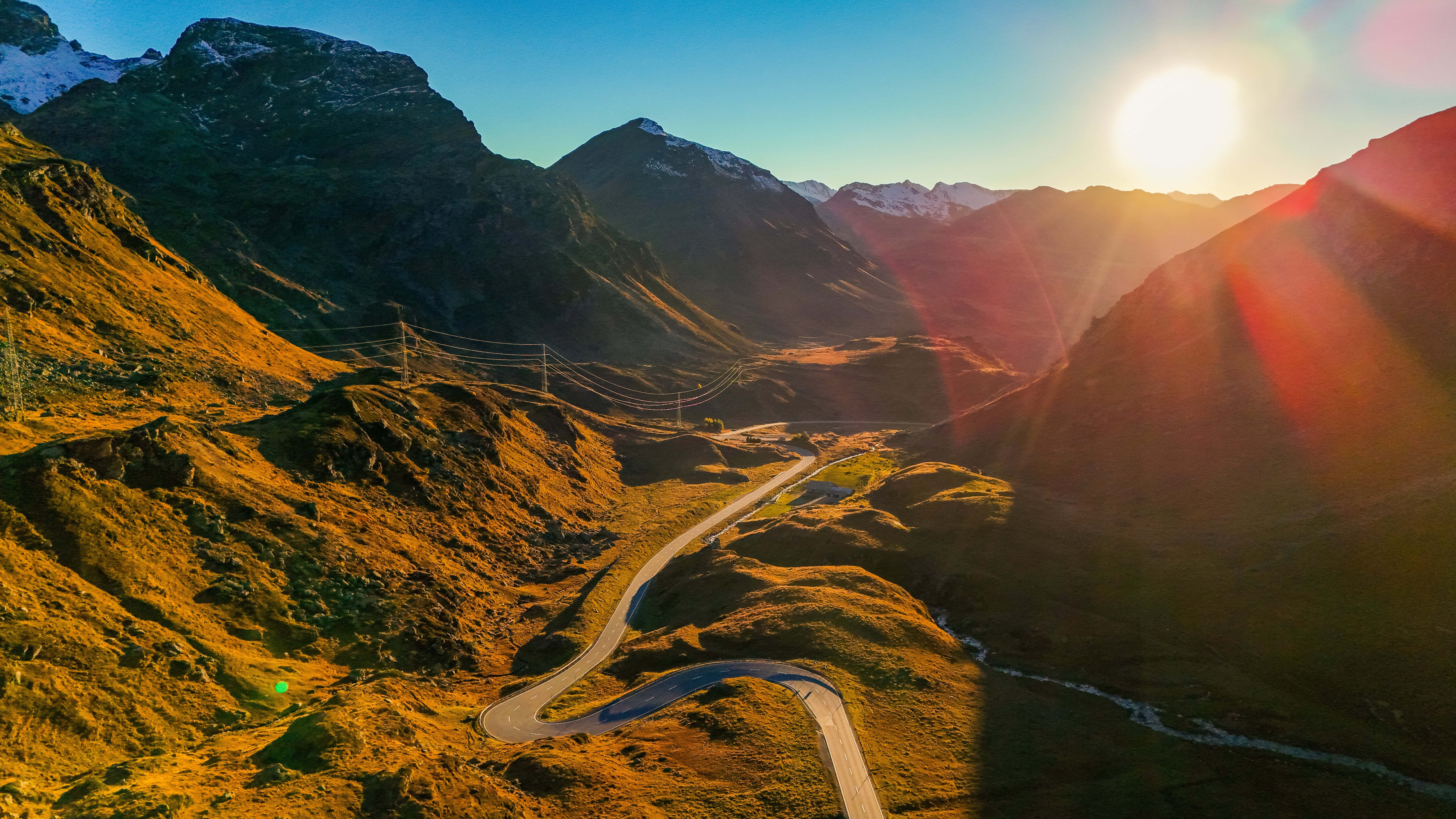 "Kurvenreiche Straße in den Schweizer Alpen bei Sonnenuntergang, umgeben von Bergen."
