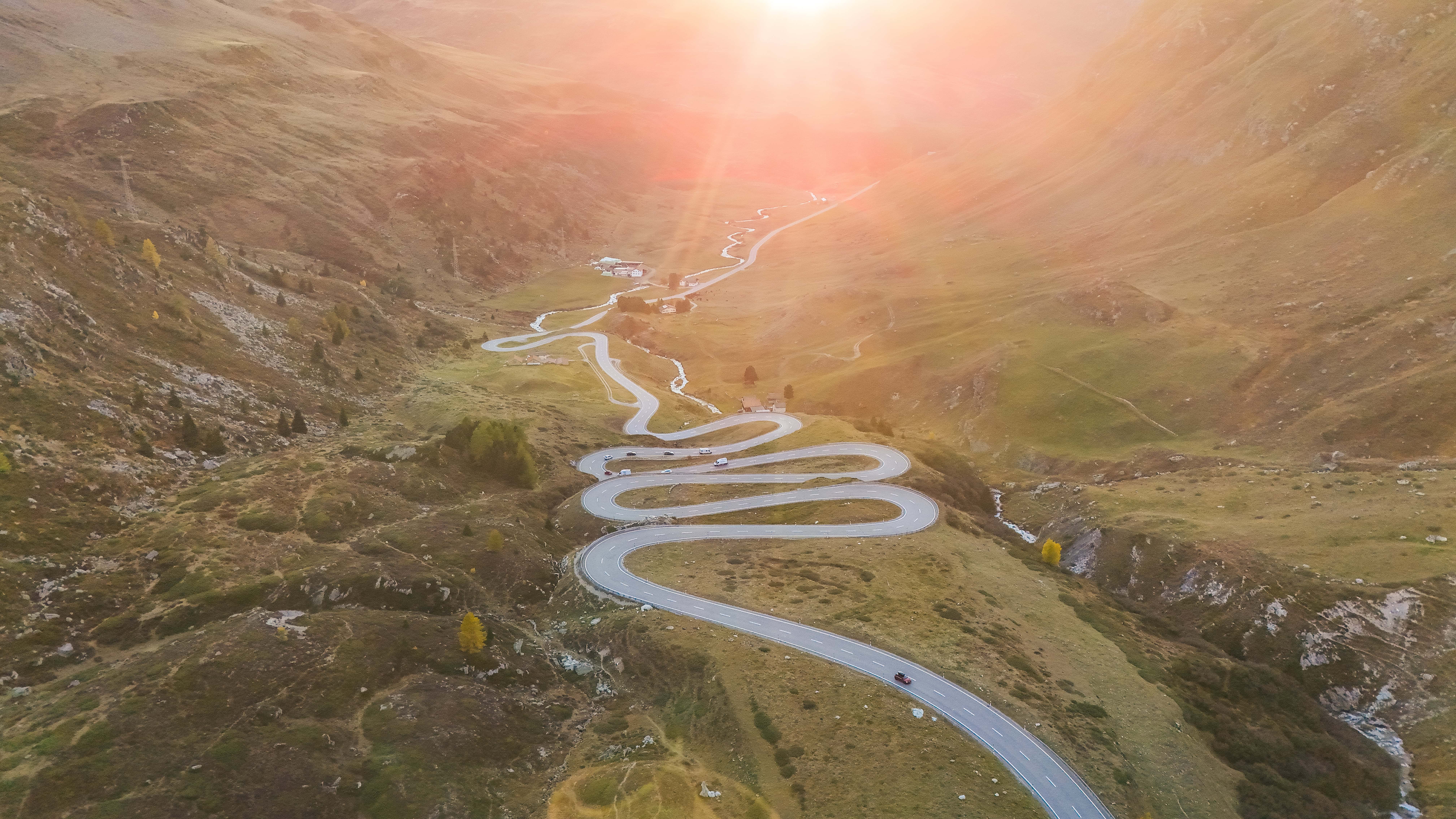 Serpentinenstraße im Sonnenaufgang durch die malerischen Alpenlandschaft.