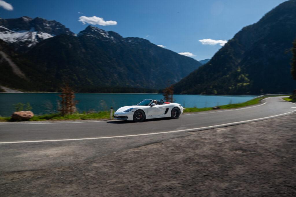 Sportwagen auf malerischer Straße entlang eines Sees in den Alpen.