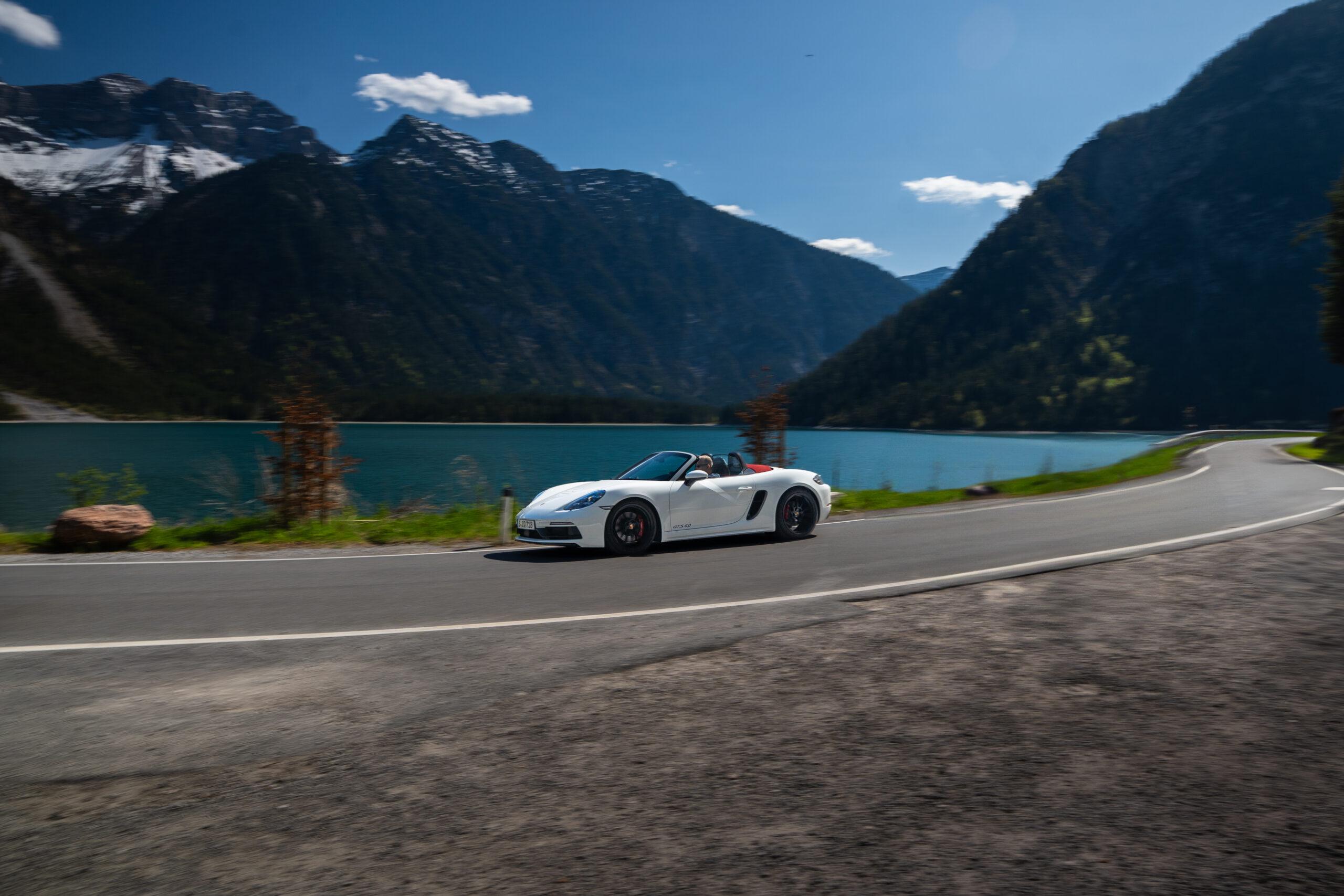 Sportwagen auf malerischer Straße entlang eines Sees in den Alpen.