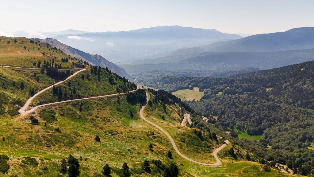 Kurvenreiche Straßen schlängeln sich durch grüne Hügel mit majestätischem Bergpanorama im Hintergrund.