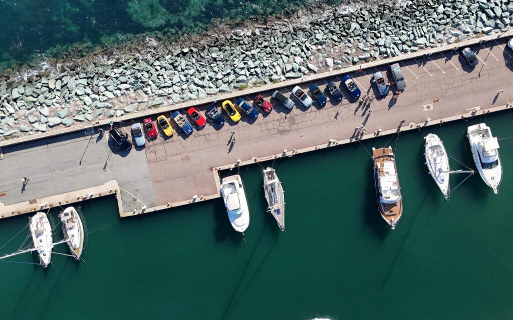 Luftaufnahme von Sportwagen am Pier neben Luxusjachten im Mittelmeerhafen.