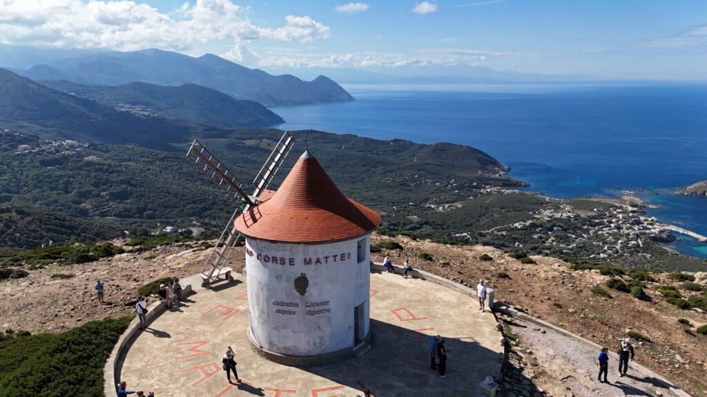Windmühle auf Hügel mit Blick auf das Meer und Berge im Hintergrund.