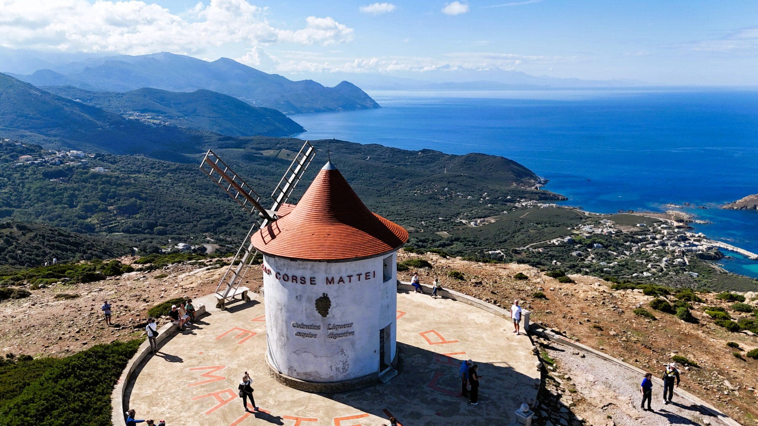 Windmühle auf Hügel mit Blick auf das Meer und Berge im Hintergrund.