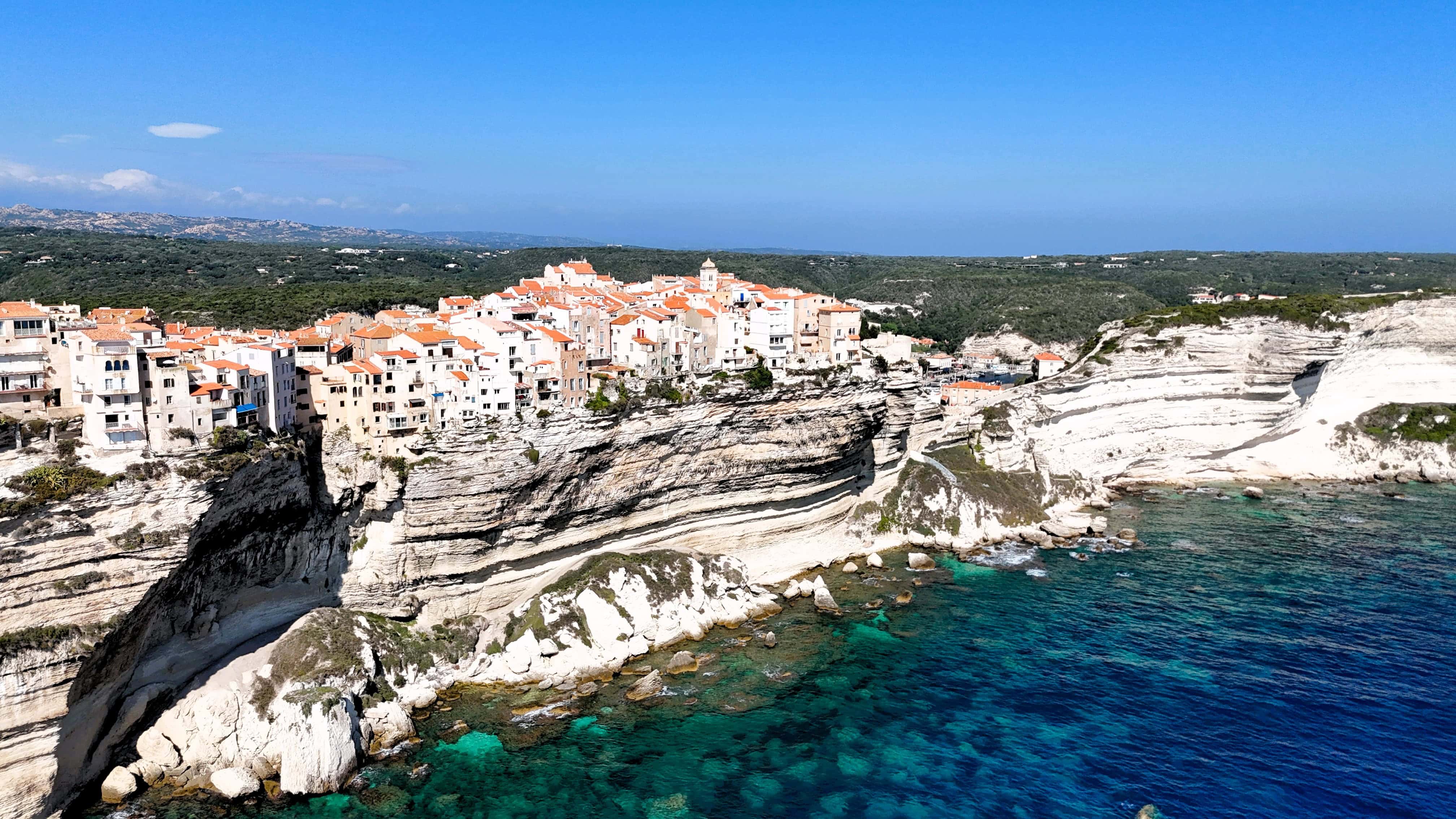 Mittelmeerklippe mit malerischer Stadt und türkisfarbenem Wasser im Hintergrund.