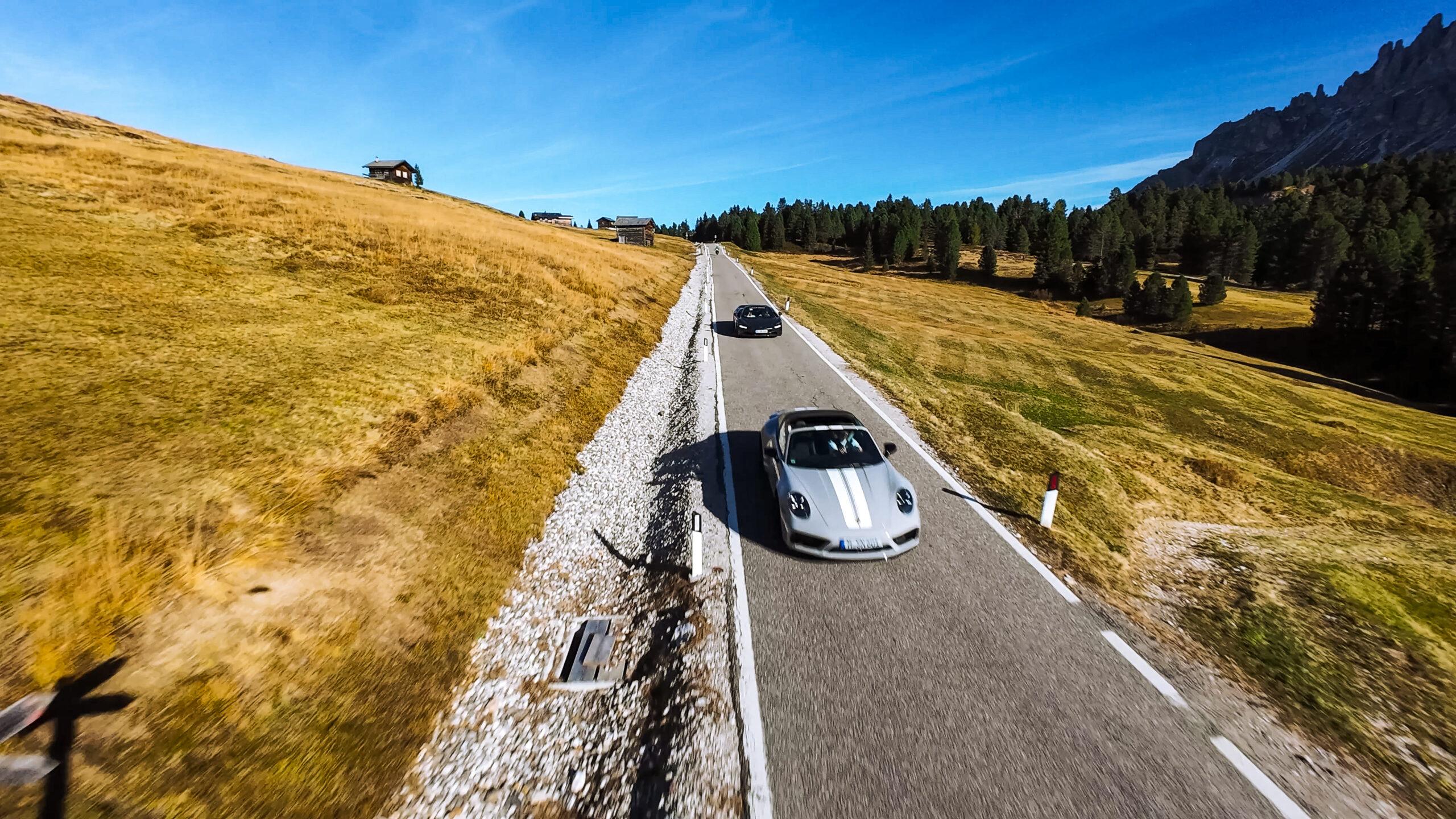 Zwei Sportwagen fahren auf einer malerischen Straße in den Dolomiten.