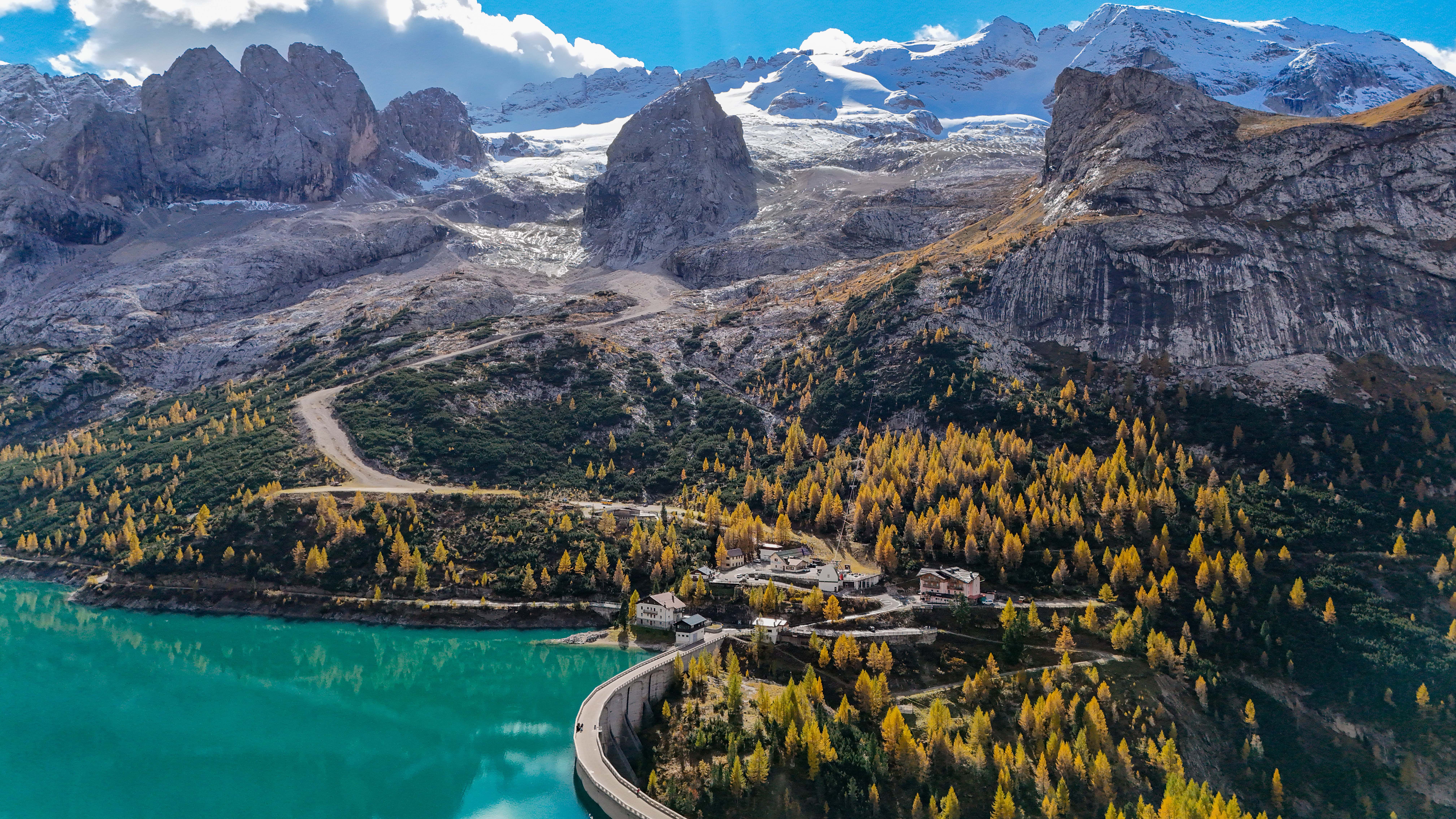 Majestätische Dolomiten über türkisblauem Wasser, umgeben von leuchtend gelben Herbstbäumen und dramatischen Gipfeln.