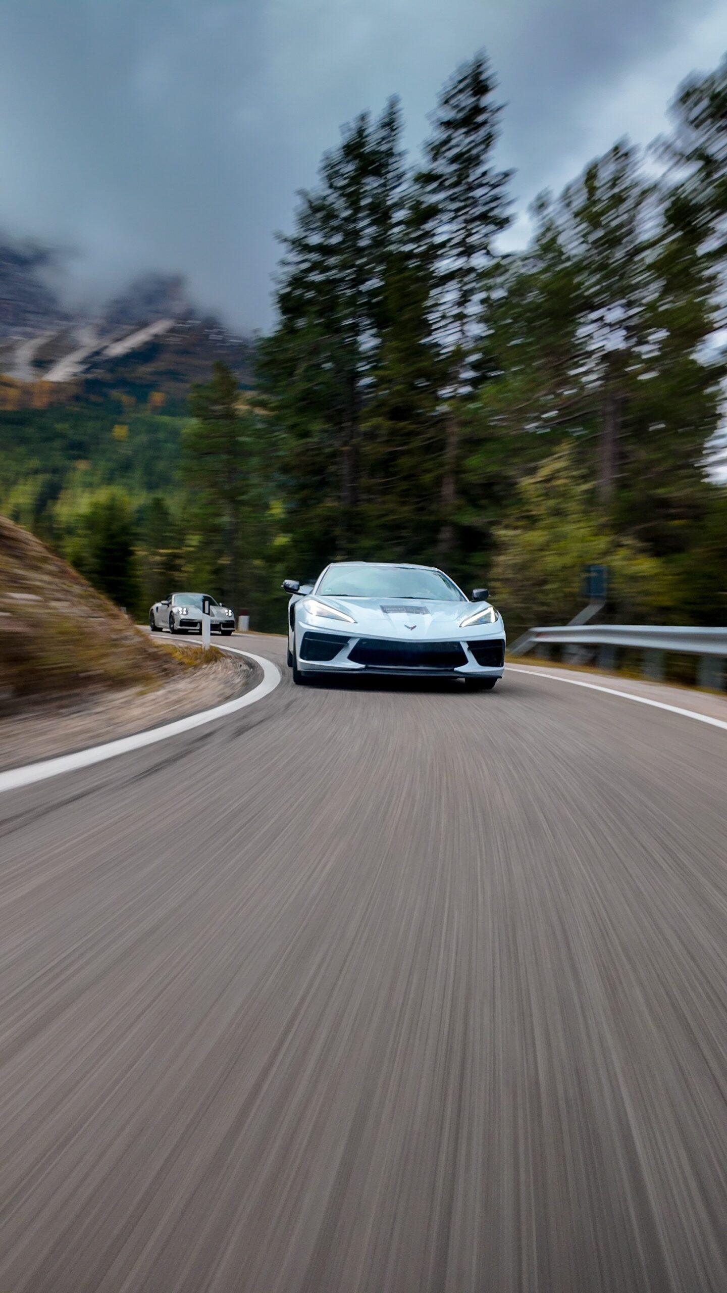 Sportwagen auf kurvenreicher Straße in den Dolomiten, umgeben von Tannenbäumen.