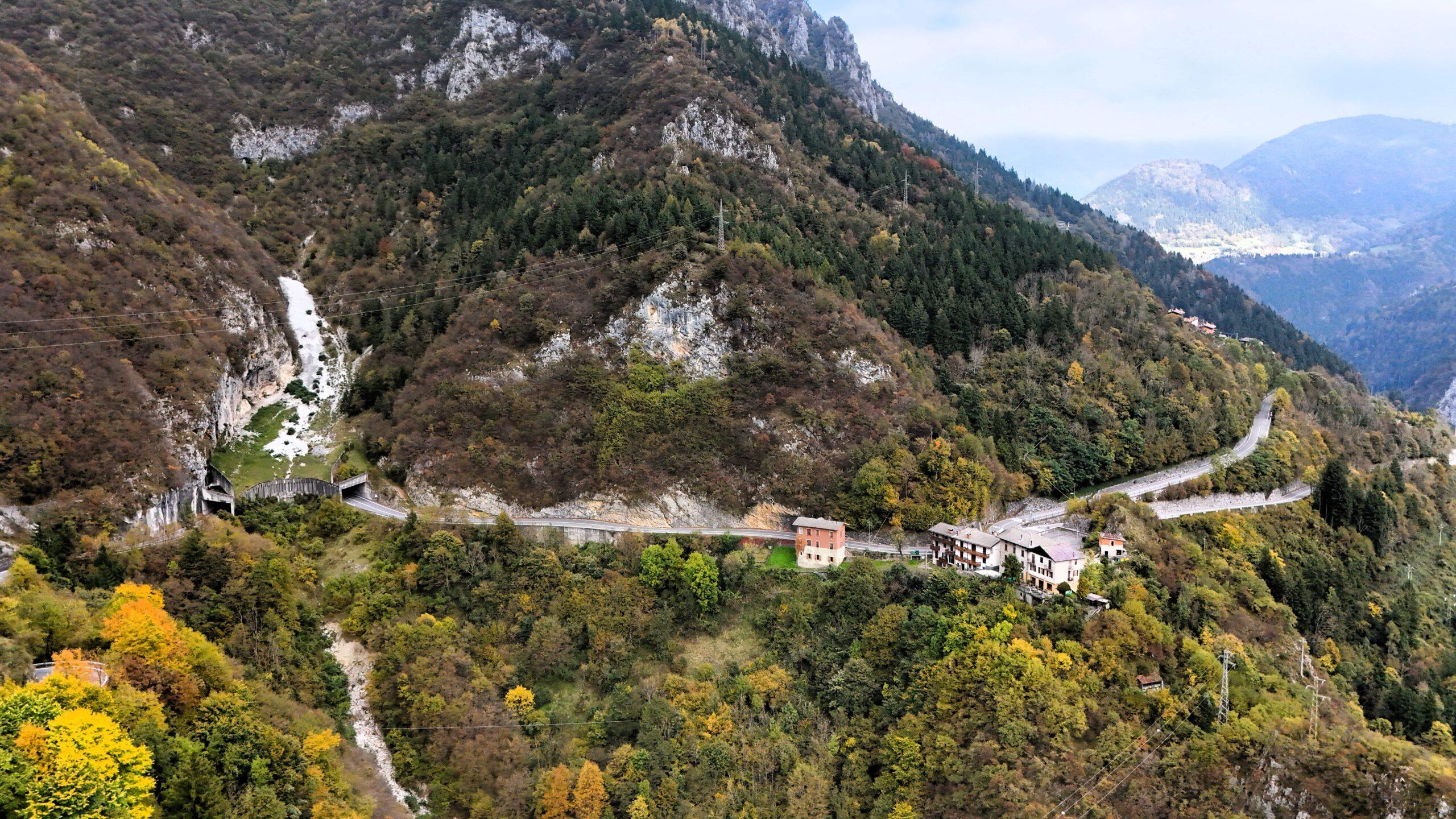 Blick auf eine kurvenreiche Bergstraße in den Dolomiten umgeben von herbstlichem Wald.