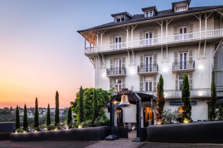 Elegantes Hotelgebäude in der Dämmerung, umgeben von Bäumen und geschmackvoller Beleuchtung. Ideal für Luxusreisen.