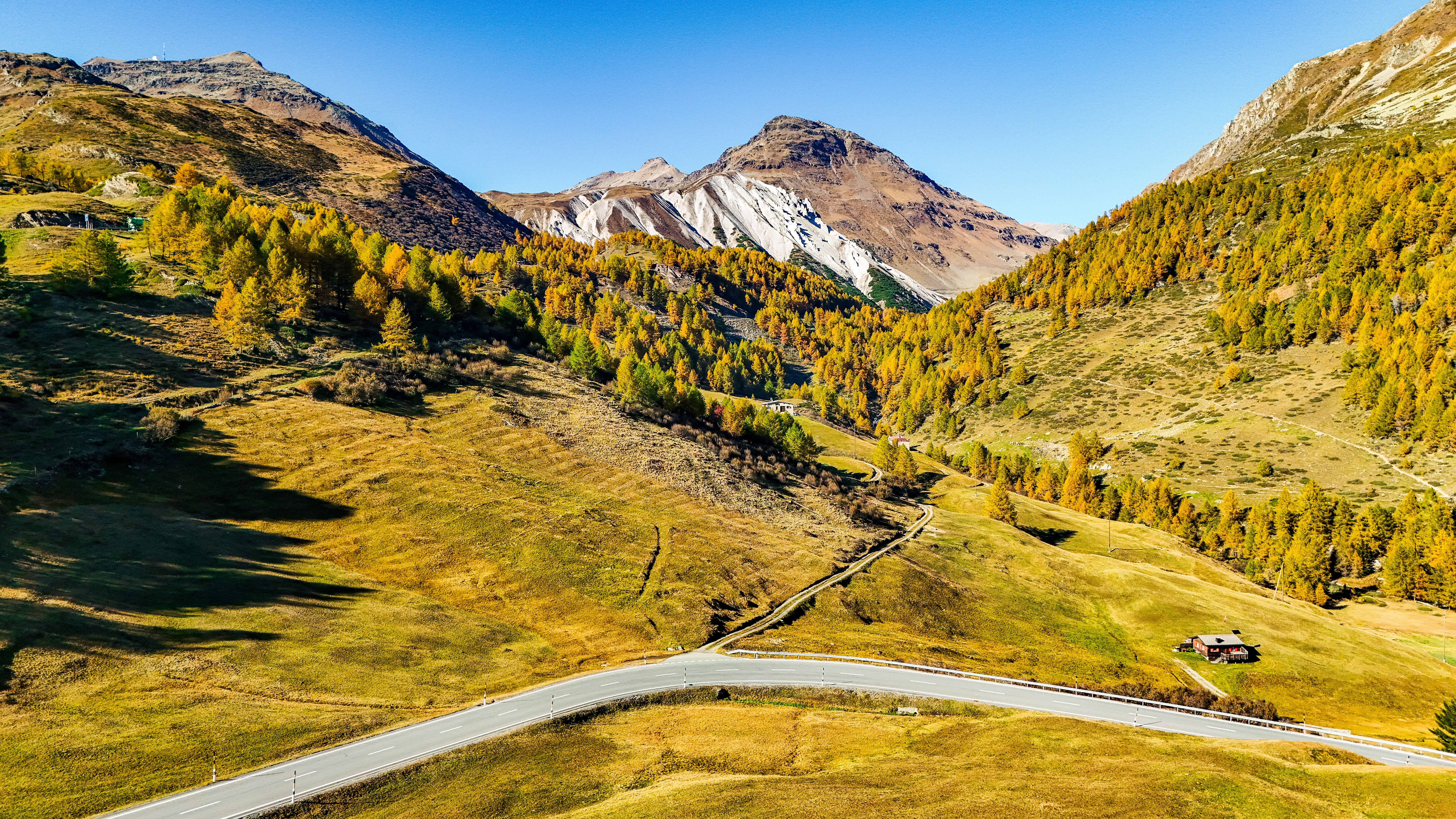 Kurvenreiche Bergstraße in den malerischen Alpen mit herbstlichen Bäumen und klarem Himmel.