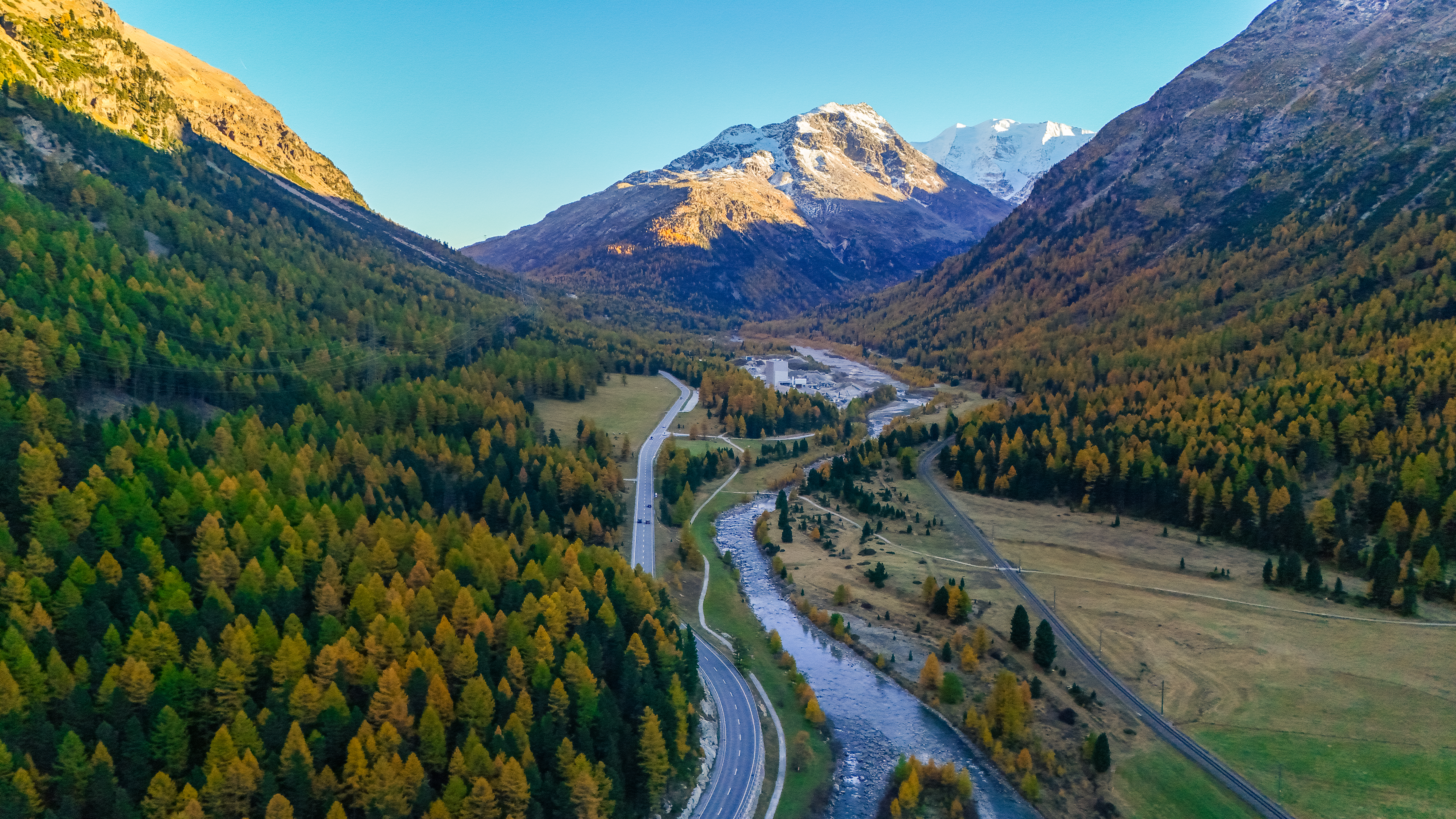 Luftaufnahme von Alpenstraße, umgeben von herbstlichen Wäldern und majestätischen Bergen.